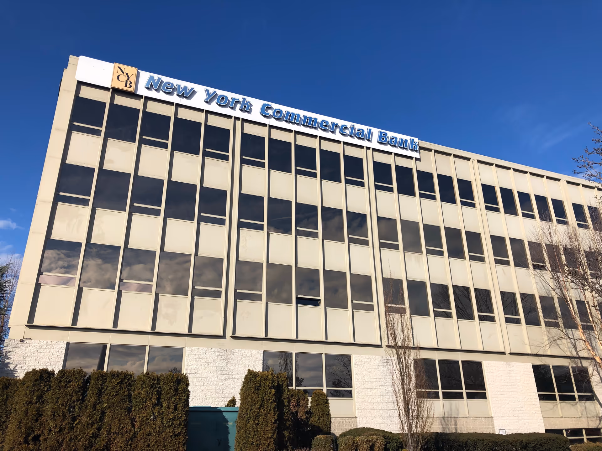 Modern glass-front office building with bank sign against blue sky.