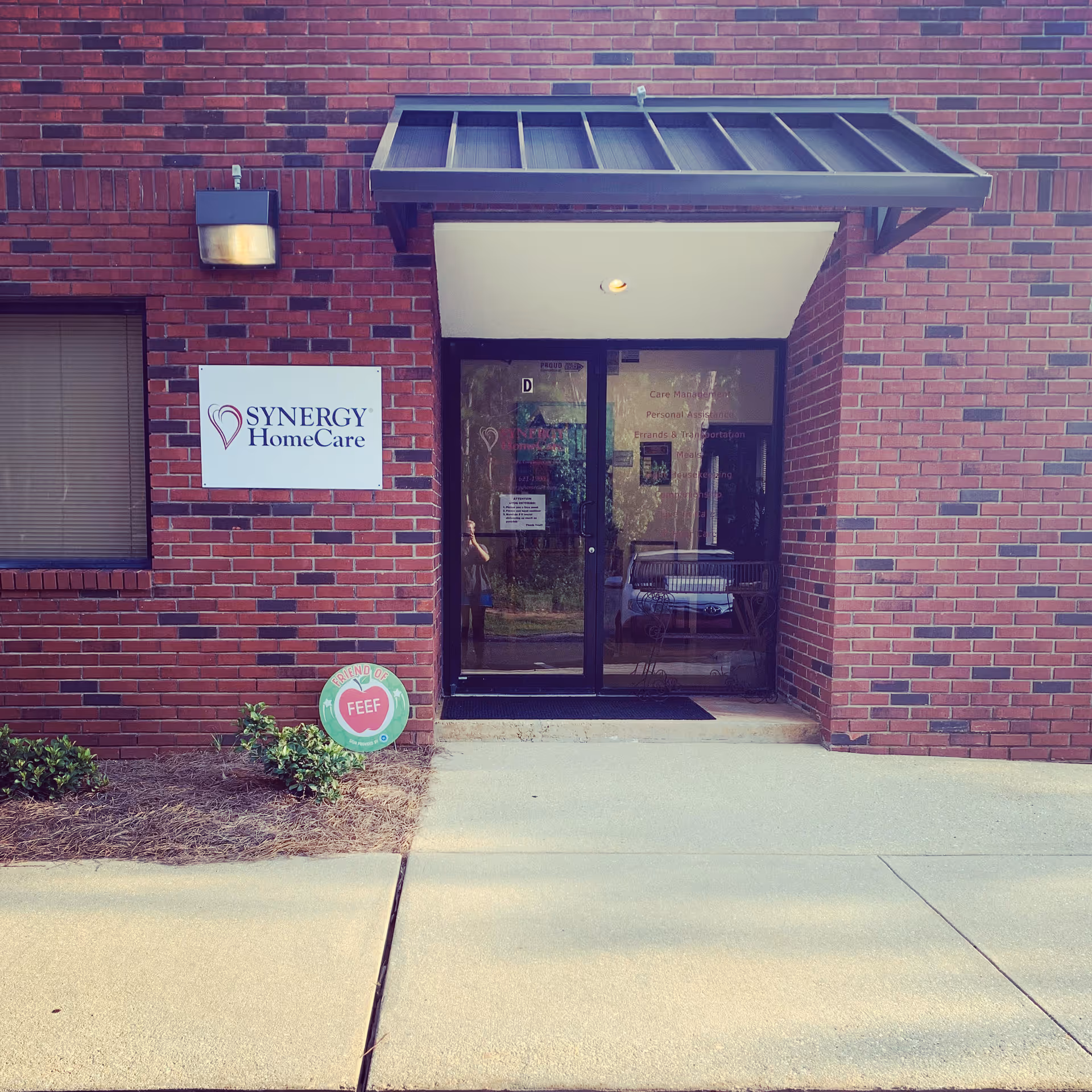 Brick exterior with Synergy HomeCare sign and glass entrance doors at the building front.