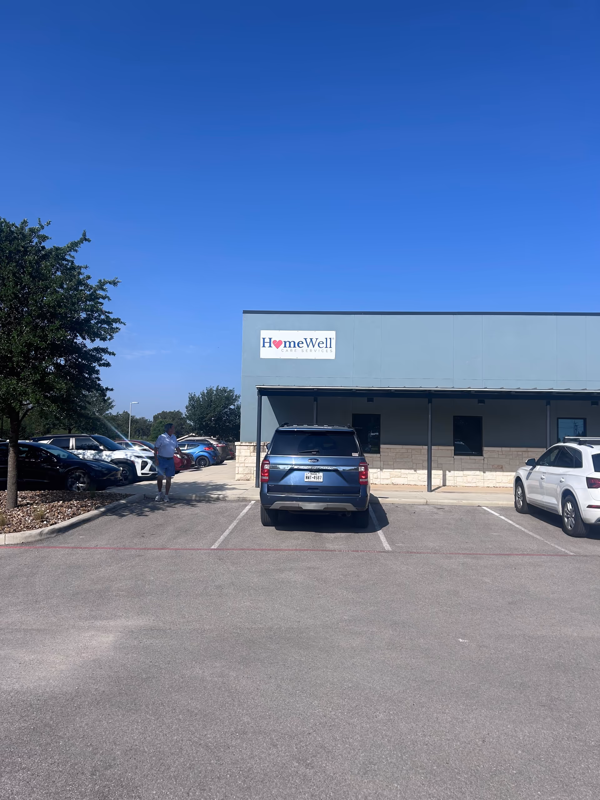 Front view of a HomeWell Care Services building with parked cars and clear blue sky.