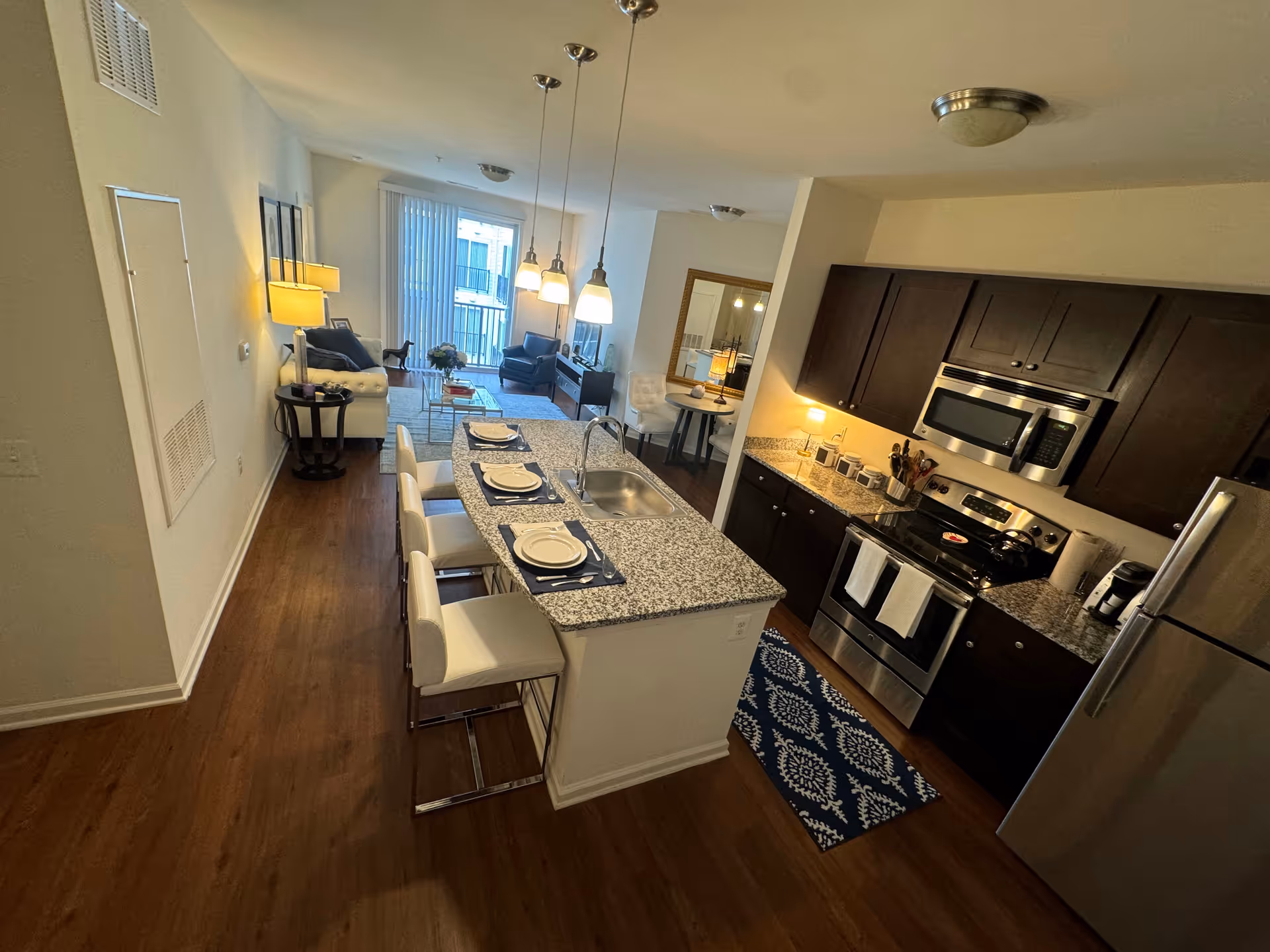 Open-concept apartment with kitchen island, granite countertops, seating area, and stainless appliances.