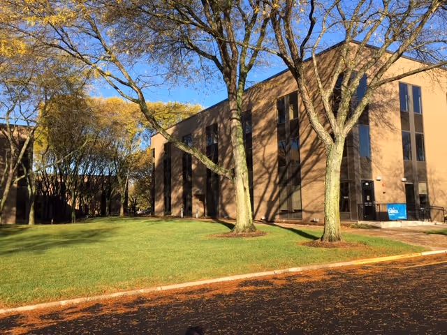 Brick senior living facility exterior with green lawn and tall trees in front.
