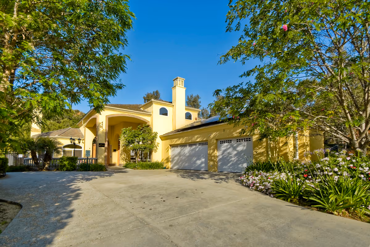 Yellow building with arched entrance, multiple garage doors, and landscaped trees along a driveway.