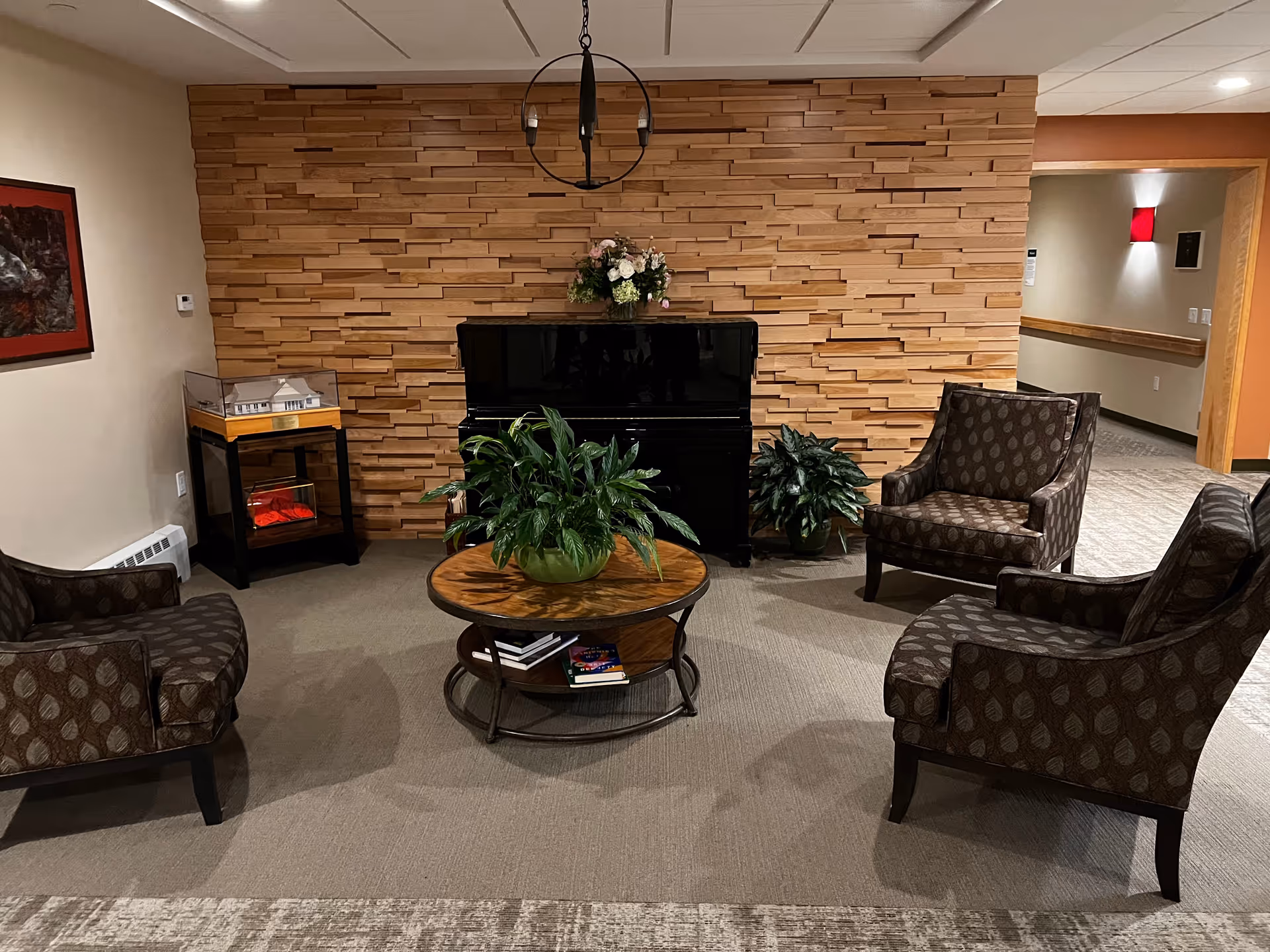 Cozy lounge with a circular coffee table, potted plants, and piano against a brick wall.