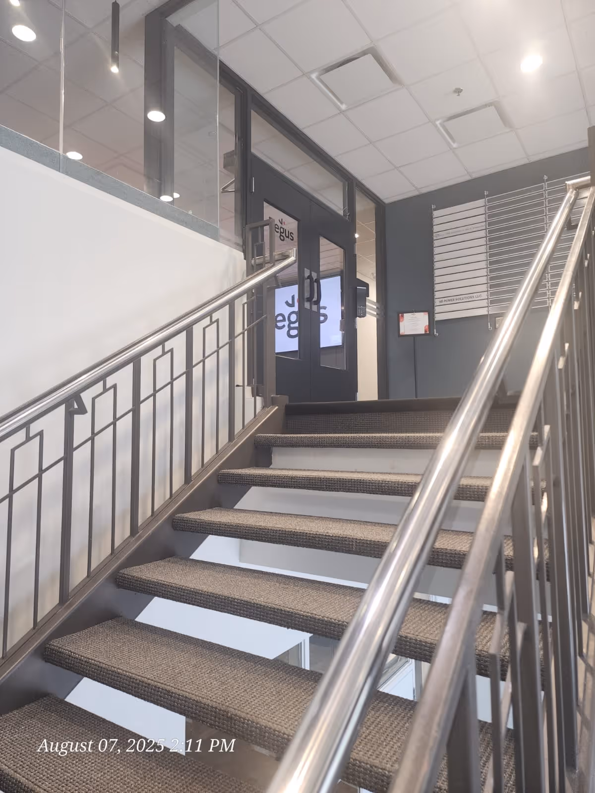 Indoor stairwell with metal railings, carpeted steps, and glass doors at the top.