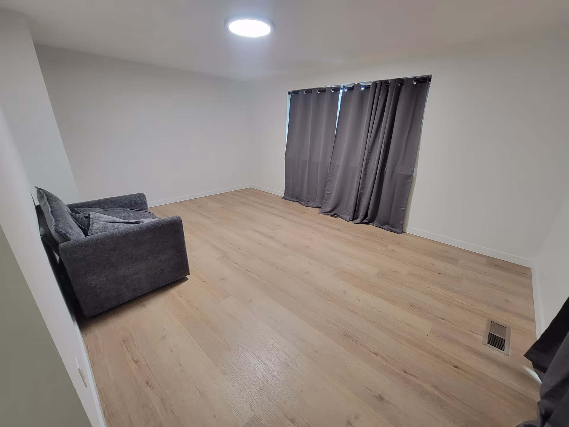 Small living room with gray sofa, dark curtains, and light wood flooring.