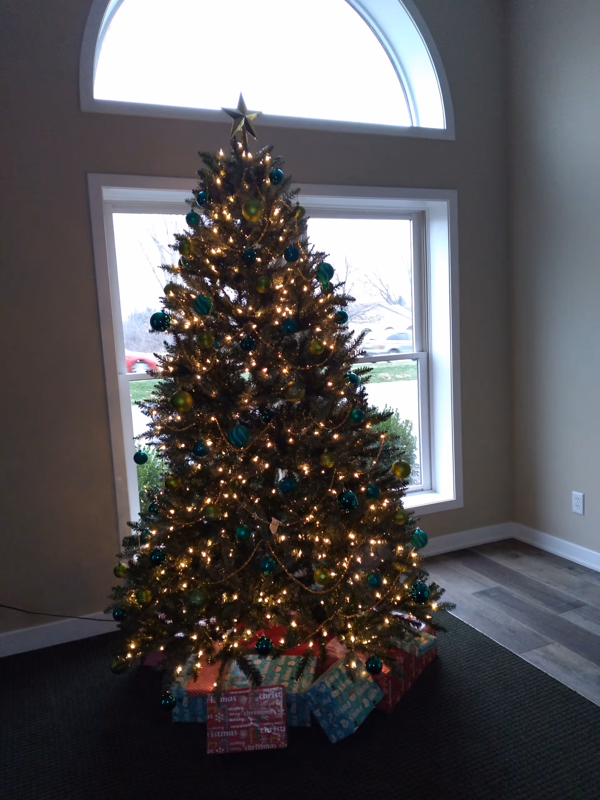 A decorated Christmas tree with lights and wrapped presents in a bright indoor room.