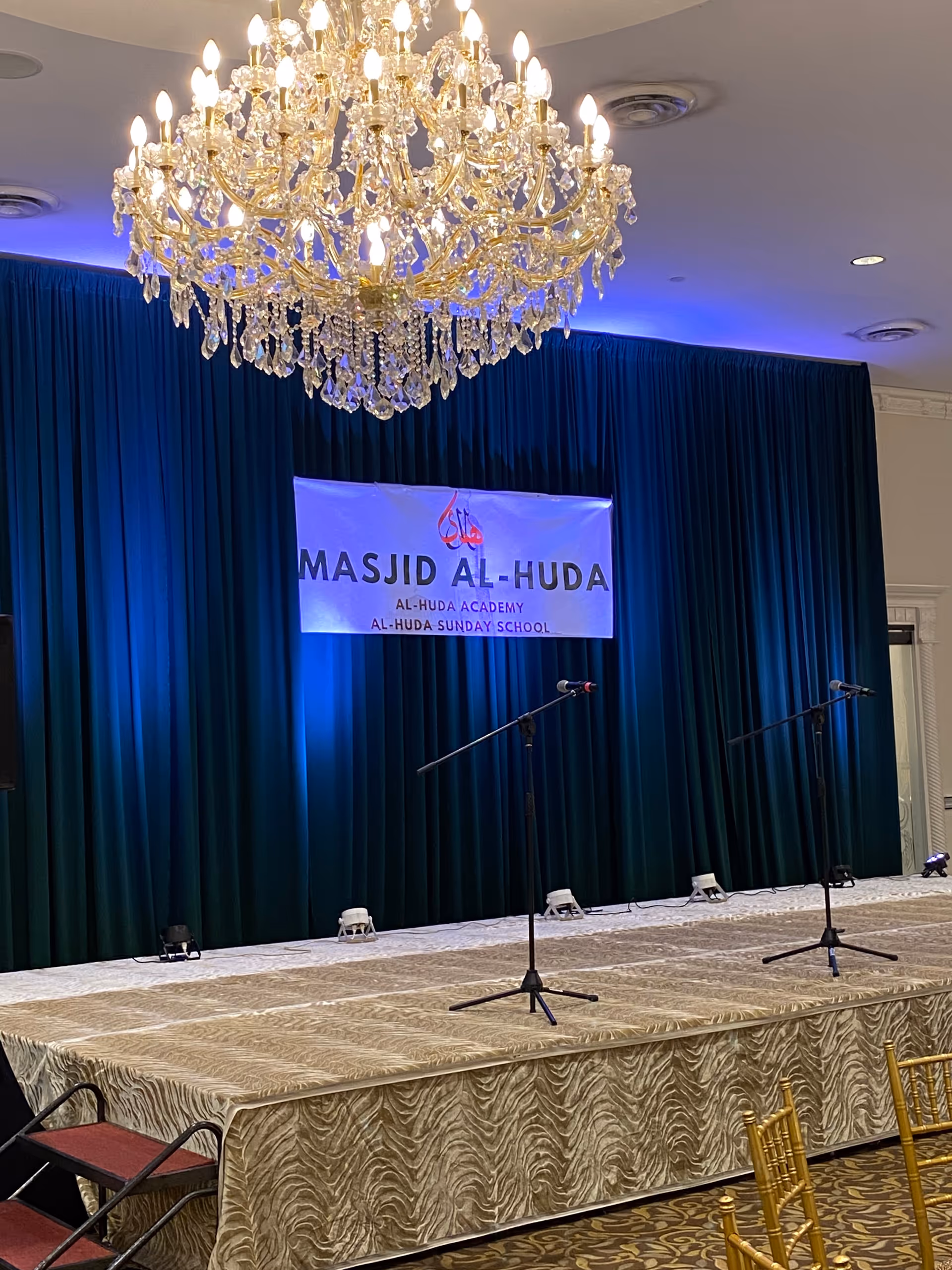 Luxurious stage with chandelier, blue curtains, and two microphone stands in an event hall.