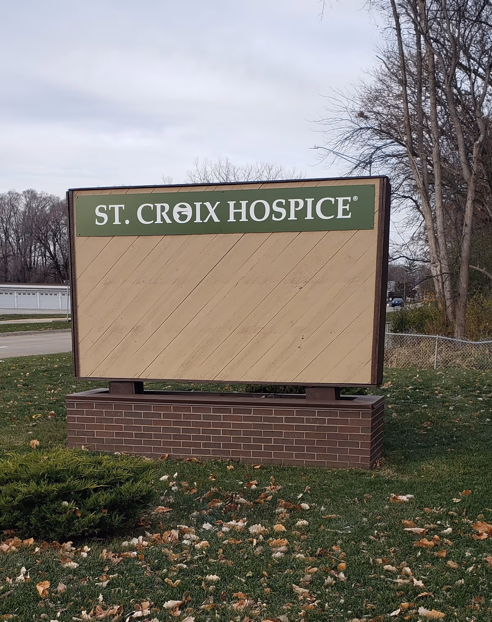 Outdoor sign reading St. Croix Hospice on brick base with grass, leaves, and bare trees.