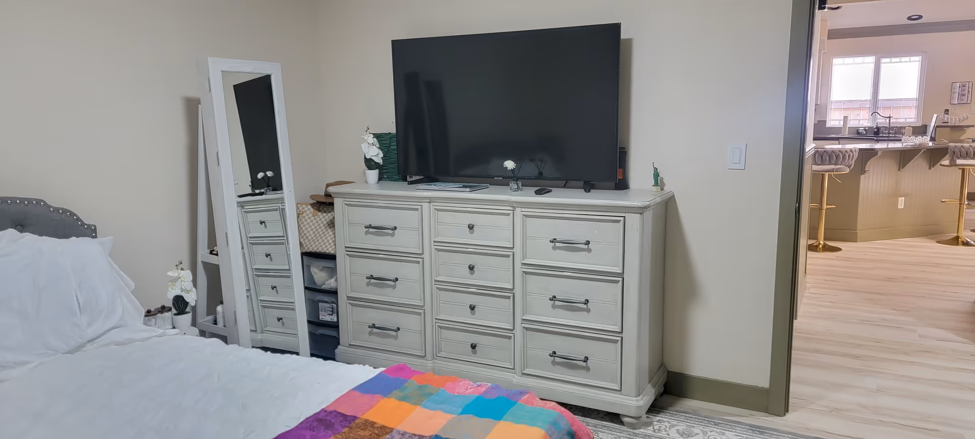 Bedroom with a dresser, TV, mirror, and doorway to the kitchen.