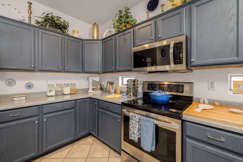 Blue kitchen cabinets surround an L-shaped counter with stove and microwave.