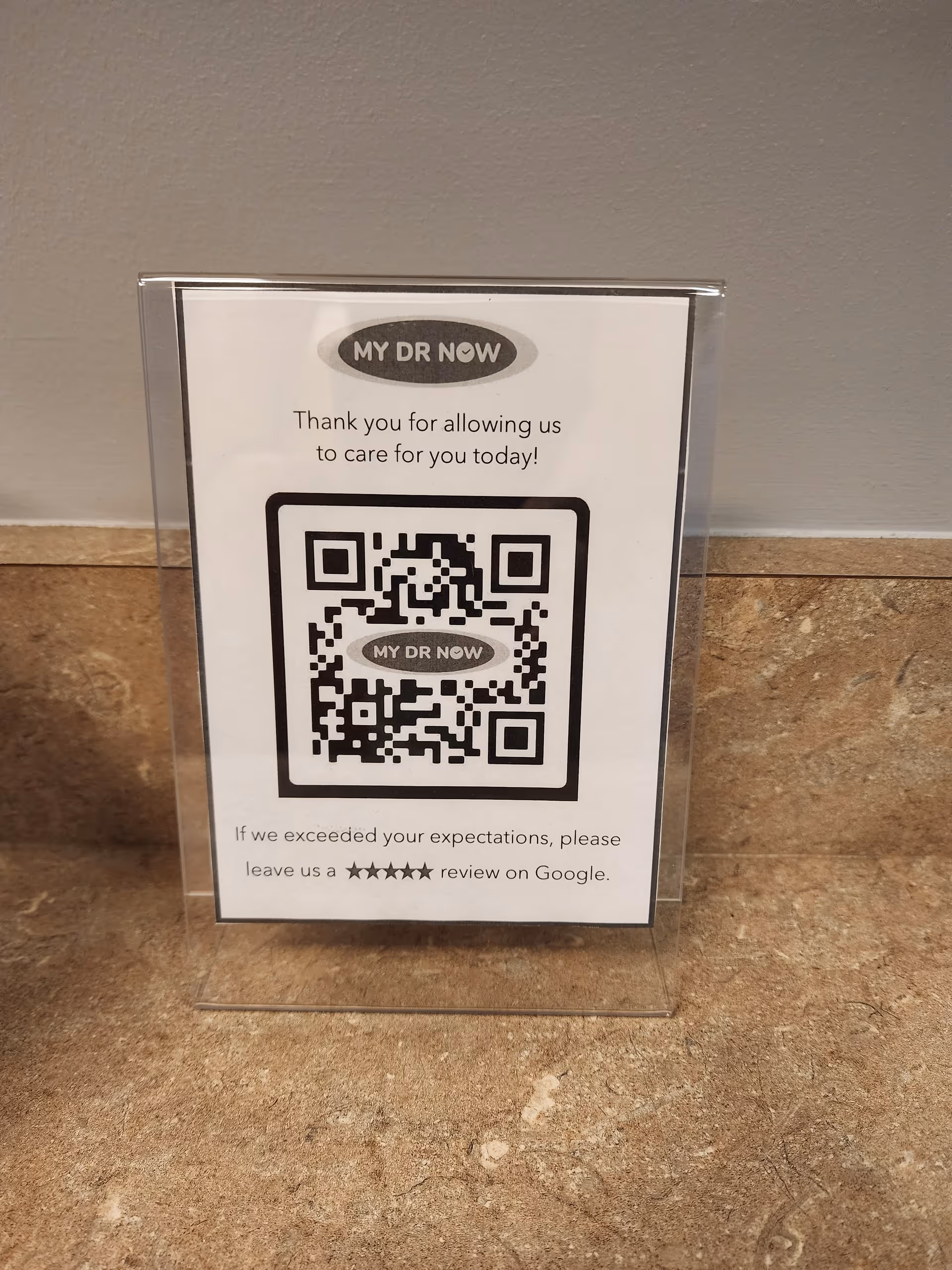A clear acrylic sign holder displays a My Dr Now QR code sign on a counter.