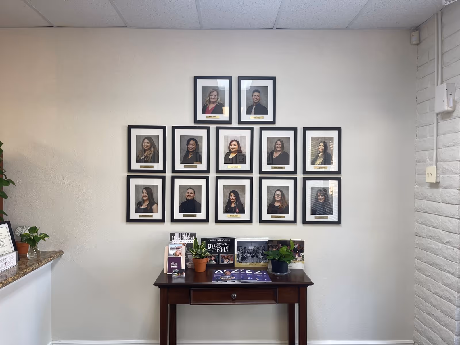 Grid of framed staff portraits on the wall above a desk in a senior living facility.