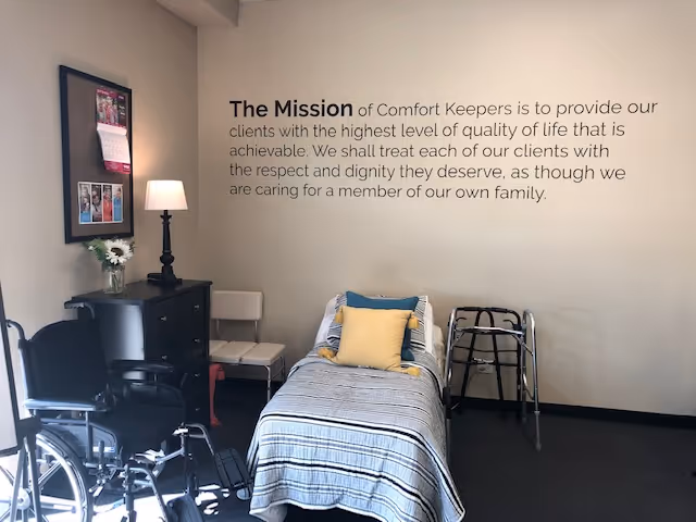 A care facility room with a bed, wheelchair, and mission statement on the wall.