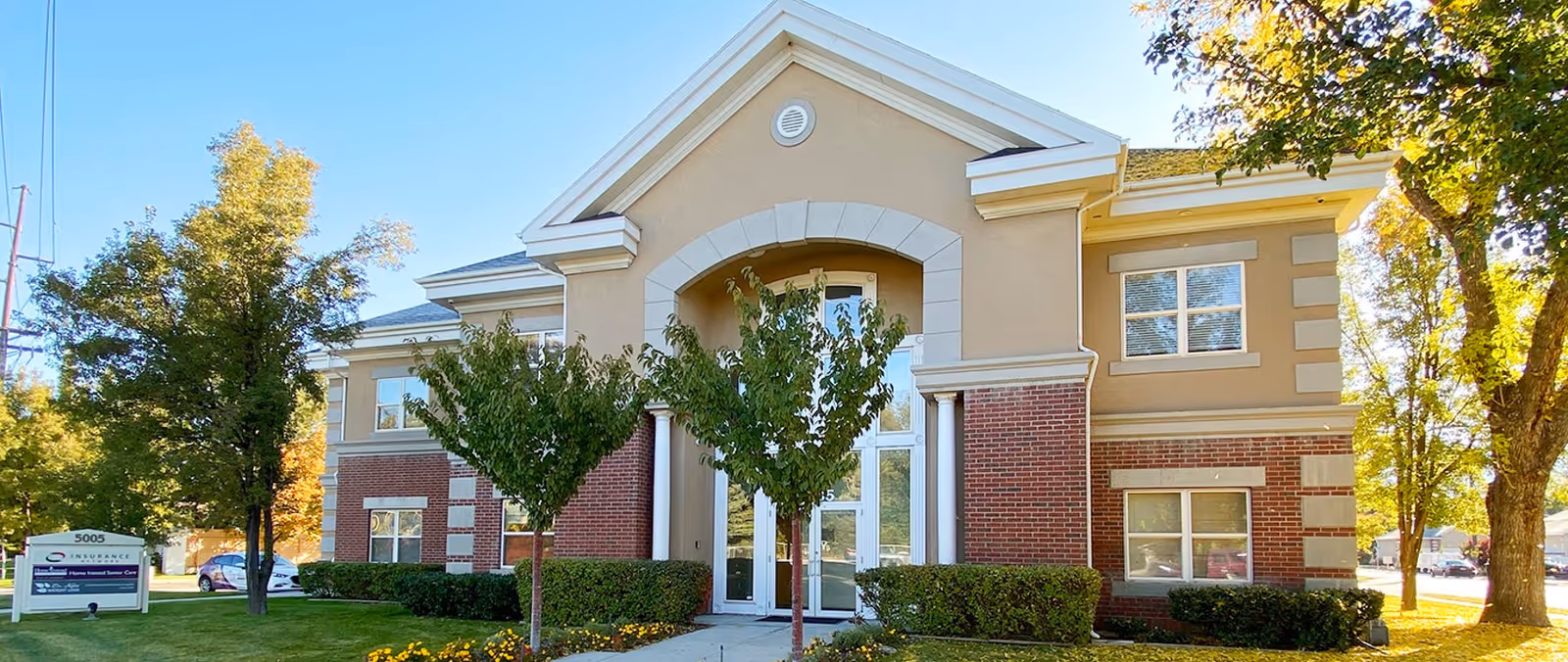 Exterior view of a Home Instead senior living facility with beige brick building and entrance arch.