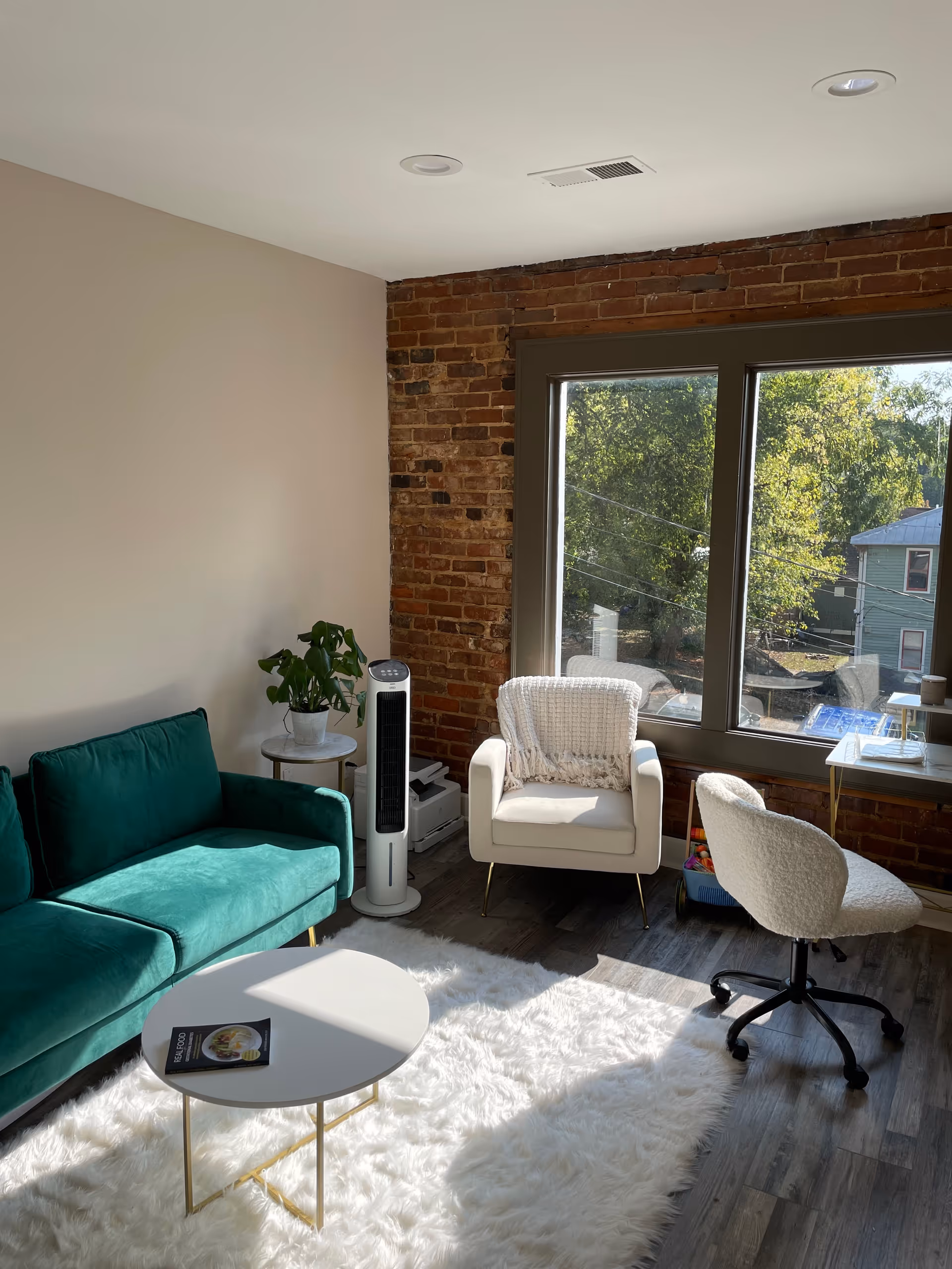 Bright modern living area with green sofa, white chairs, brick accent wall, and window.