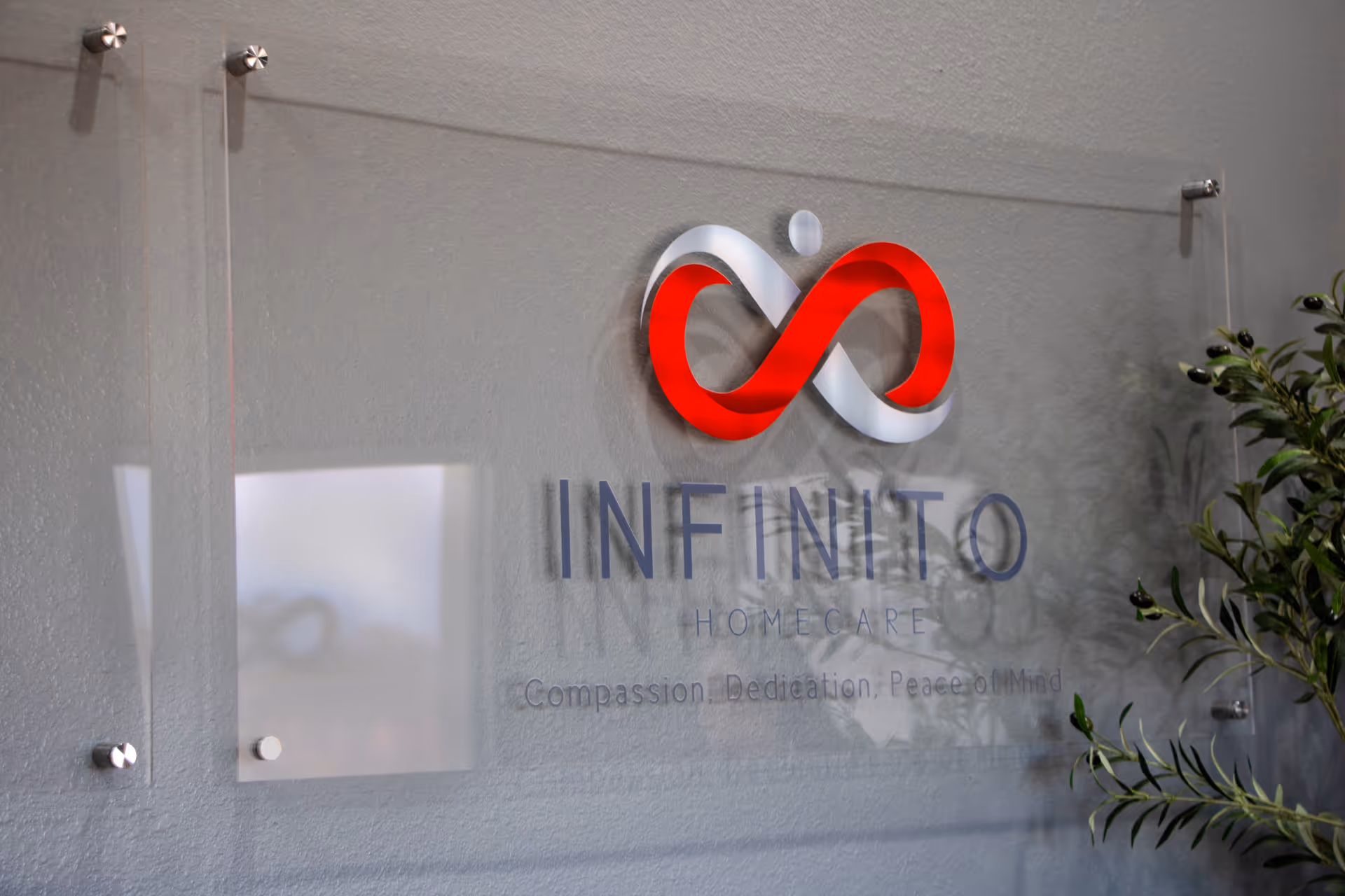 Interior wall plaque featuring Infinito Homecare logo and name beside a decorative plant.