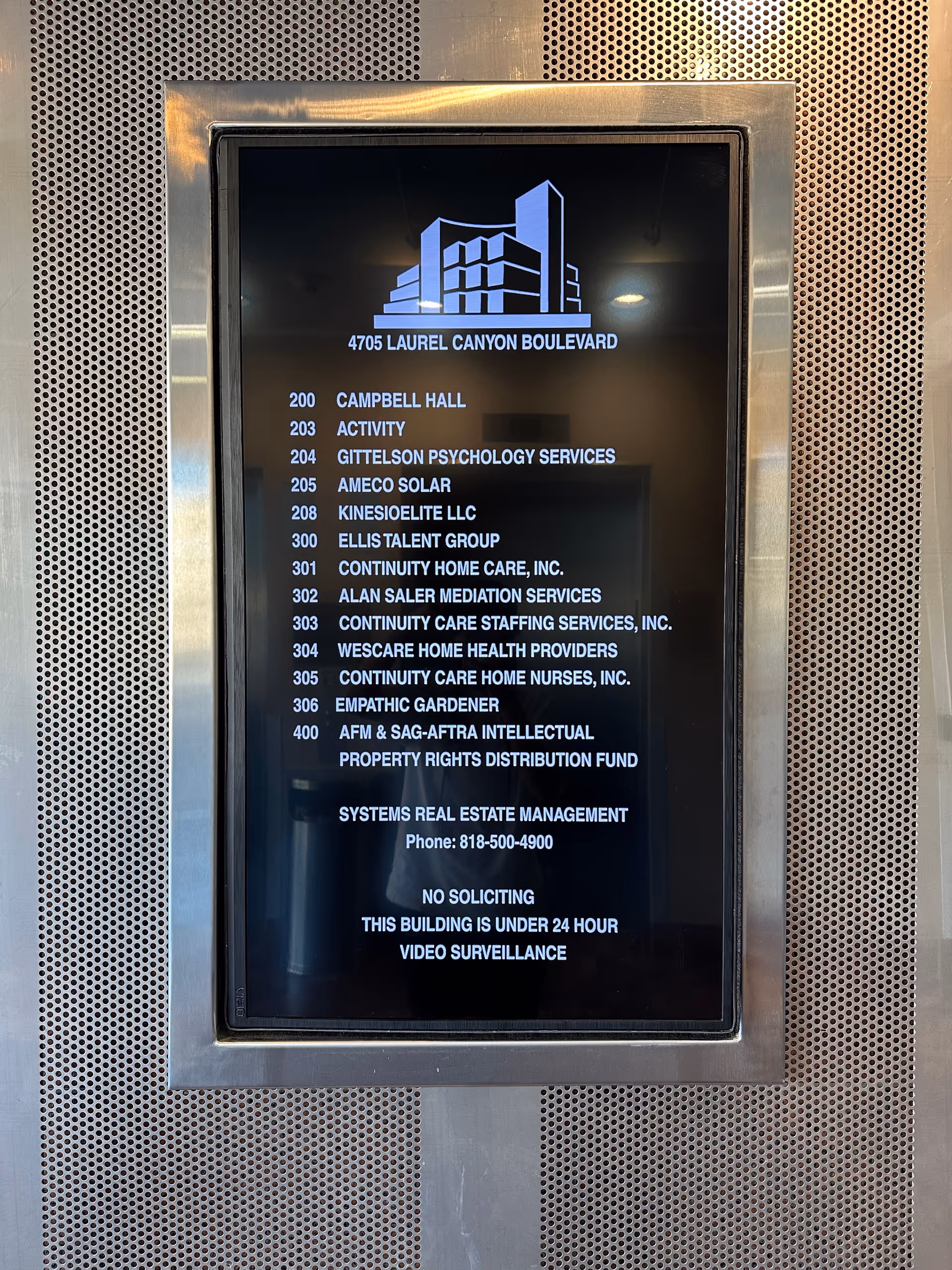 Digital directory screen listing tenants and address on a metal interior wall.