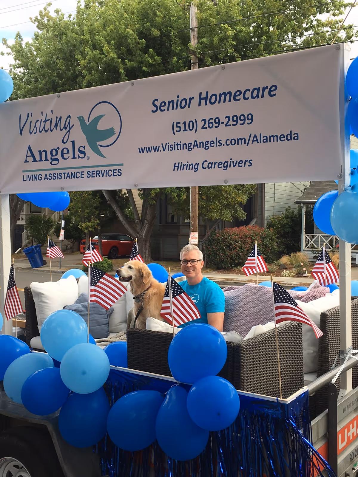 Parade float promoting Visiting Angels Senior Homecare with man, dog, and blue balloons.