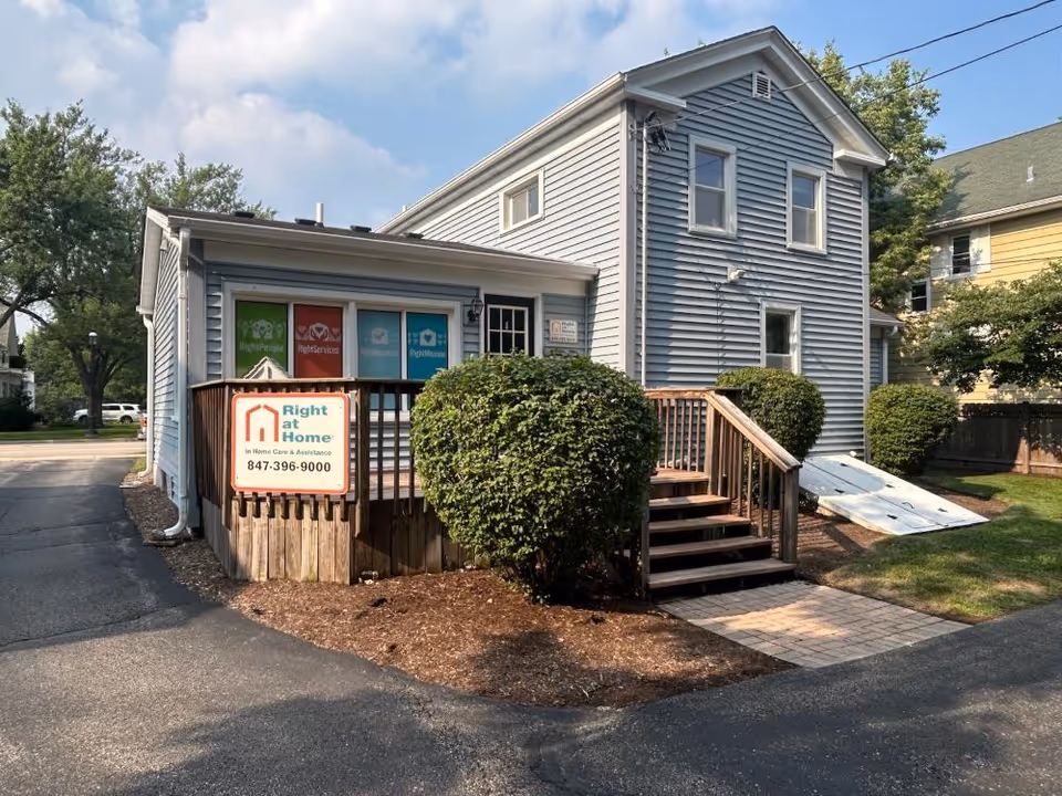 Blue two-story building with a ramp, Right at Home sign, and neatly trimmed hedges.