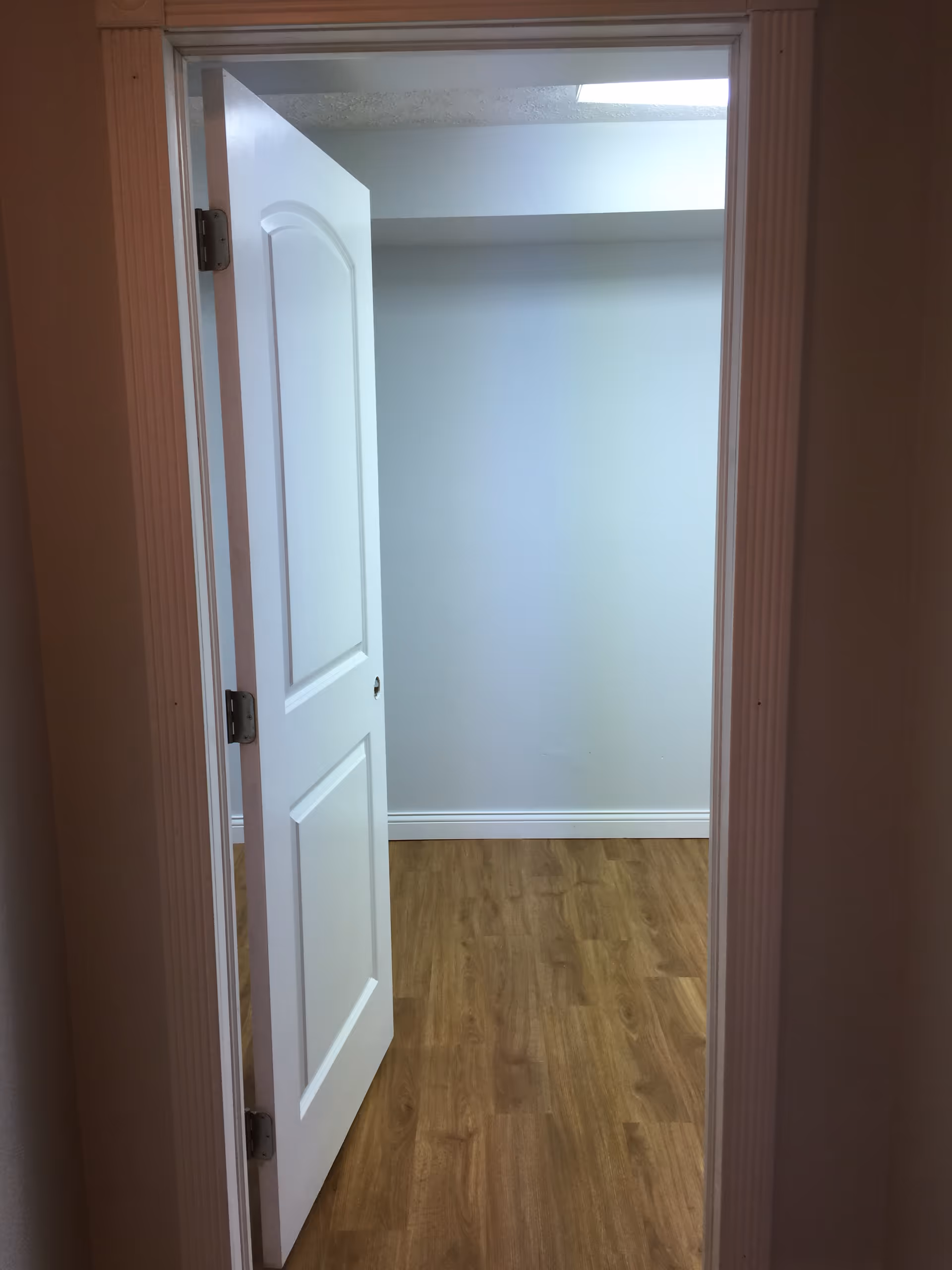 Open white door reveals a small empty room with light gray walls and wood floor.