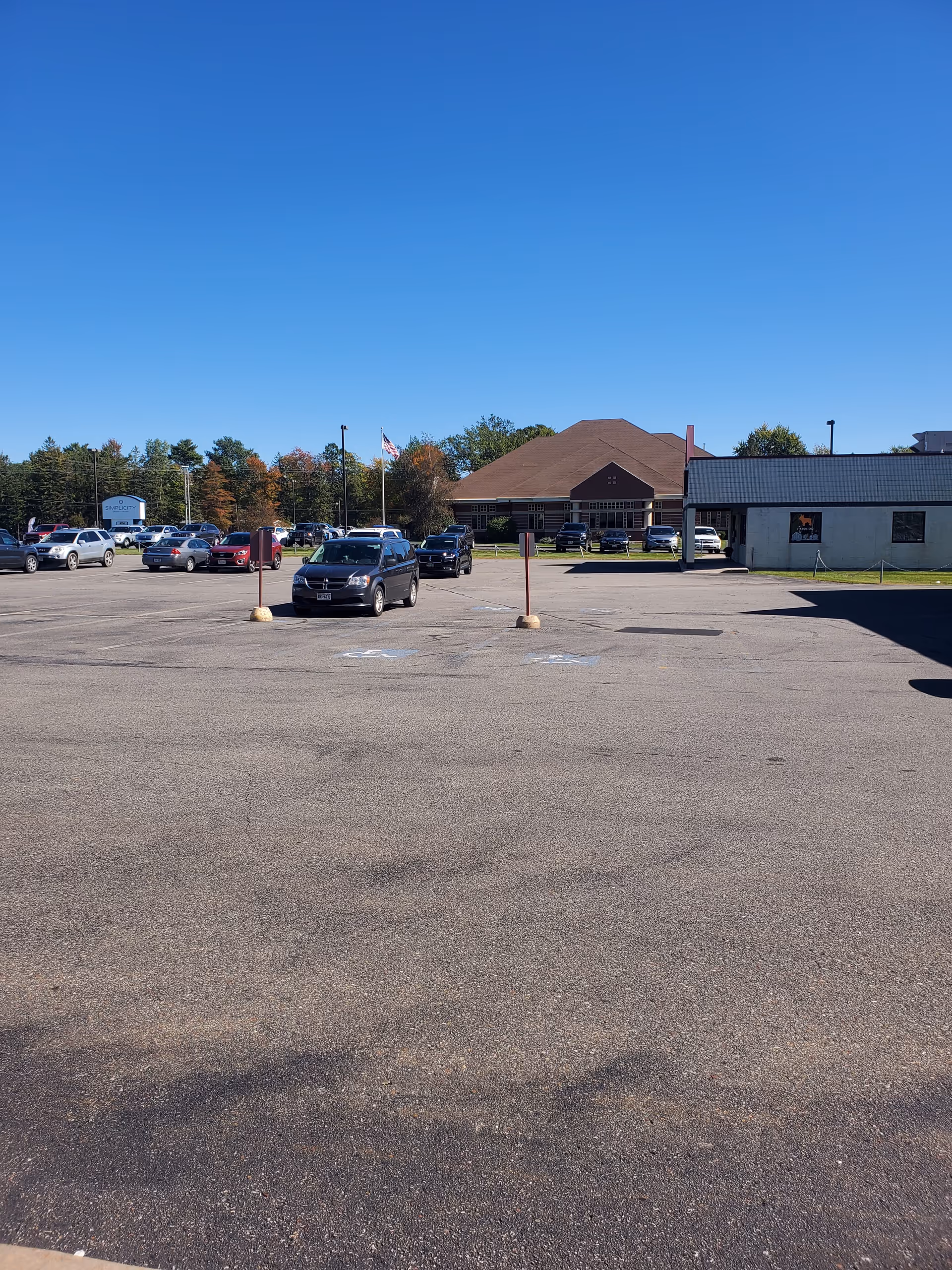 Wide parking lot with several cars and a brown-roofed building in the distance.