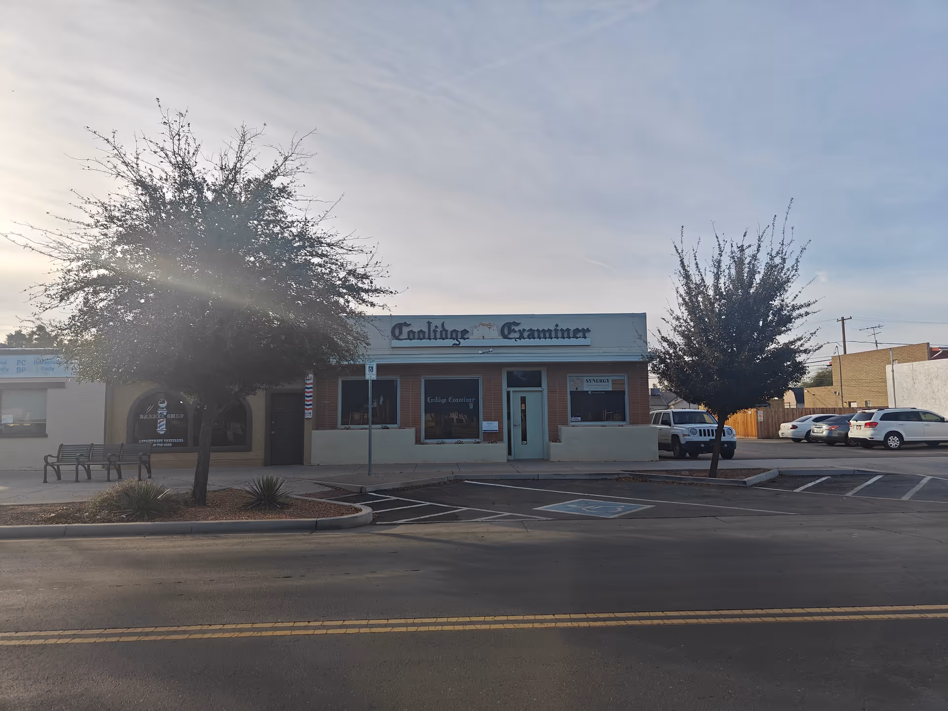 One-story brick storefront with sign, trees, and a parking lot.