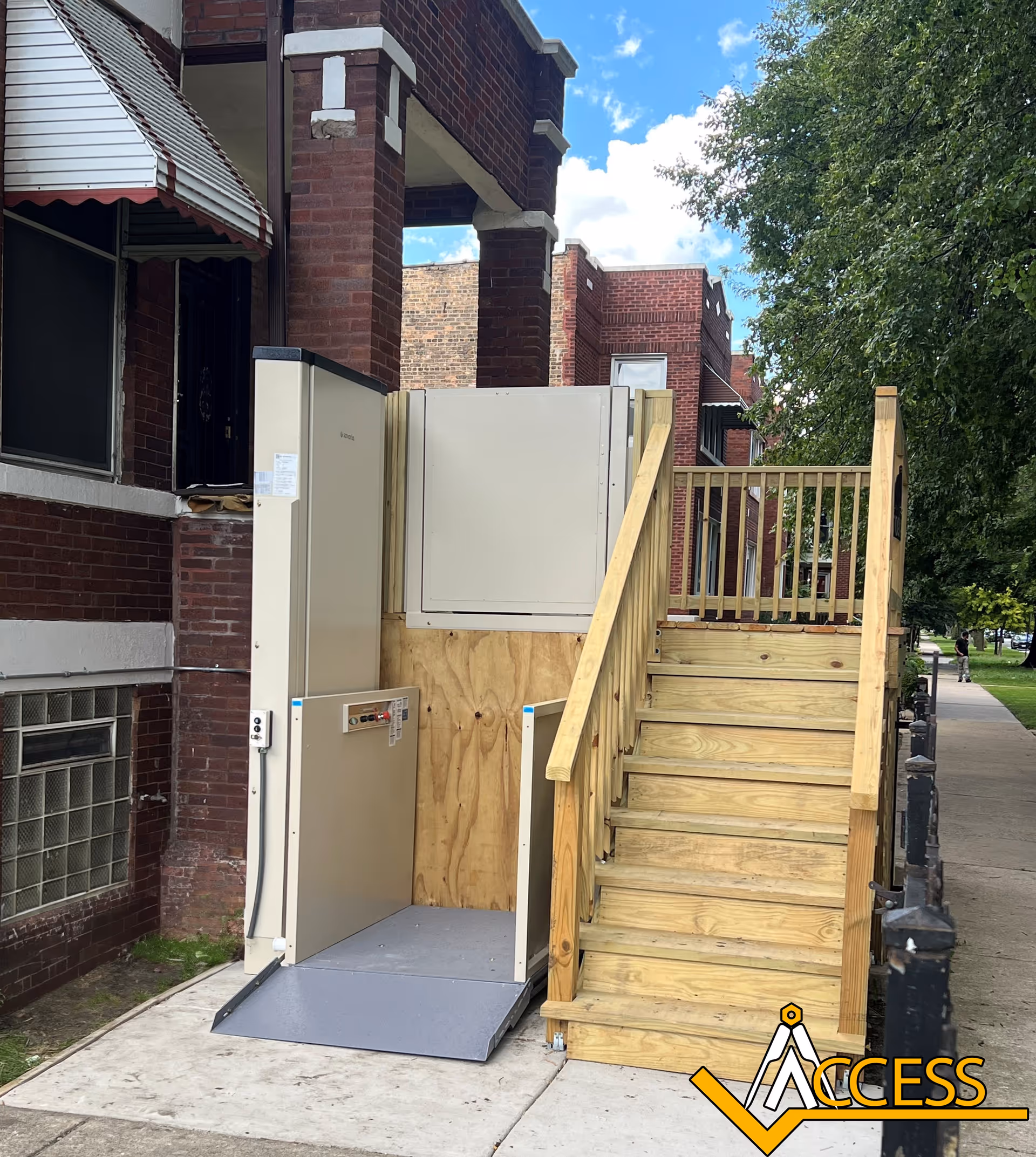 Exterior view of an elevator platform with wooden ramp beside brick building.