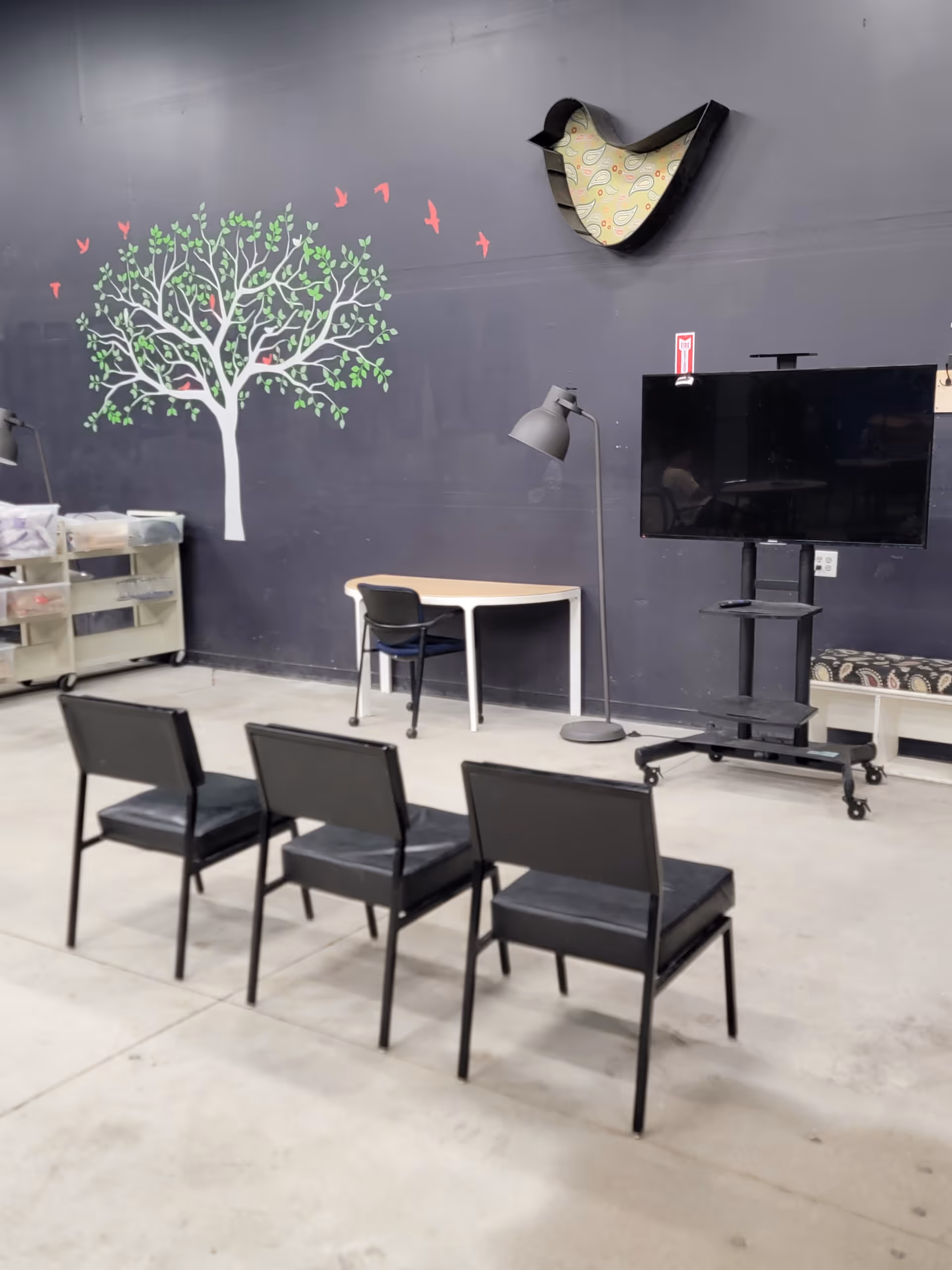 Empty activity room with four black chairs facing a mounted TV and mural wall