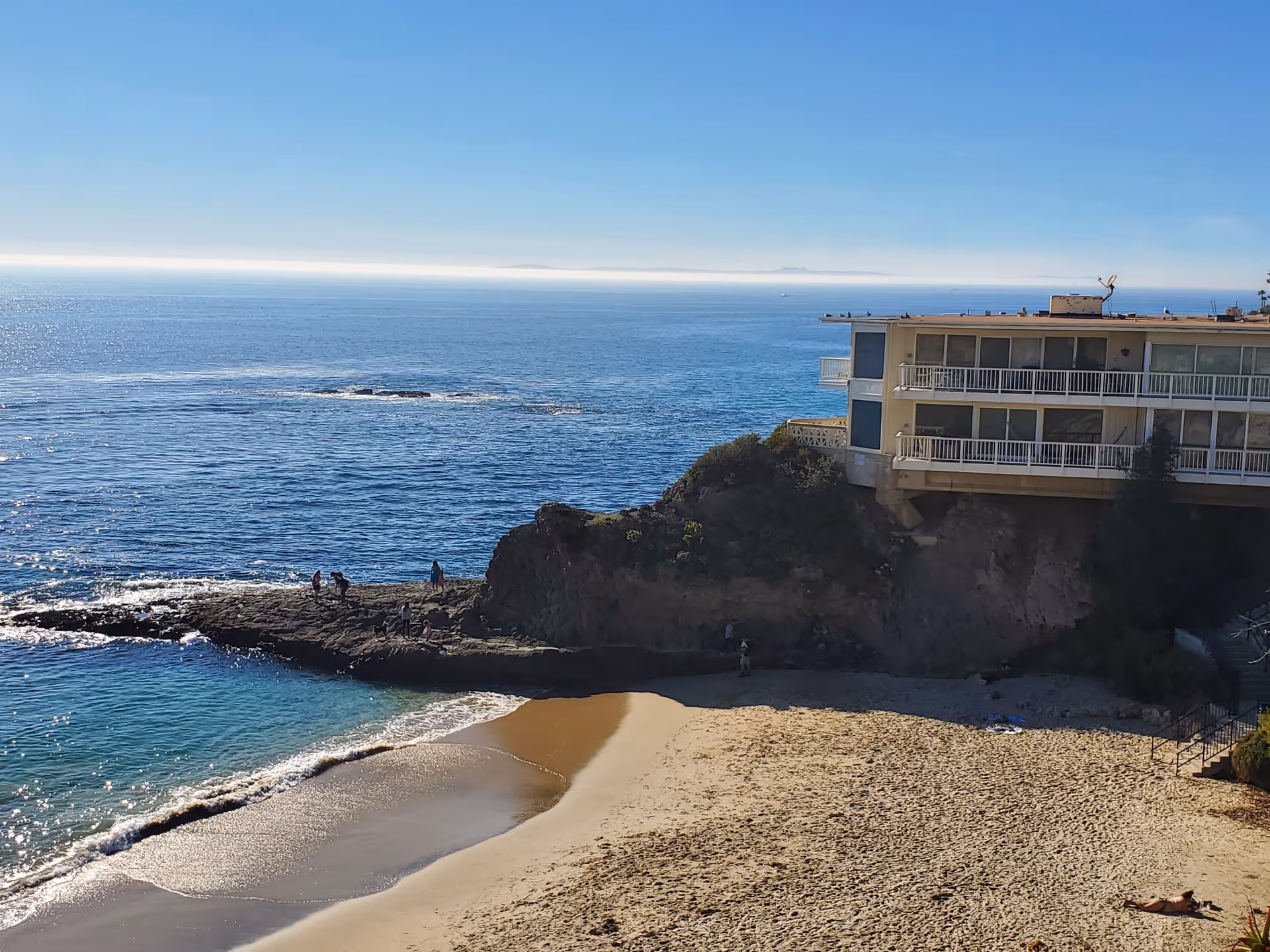 Coastal view shows a seaside senior living building perched above a sandy beach.