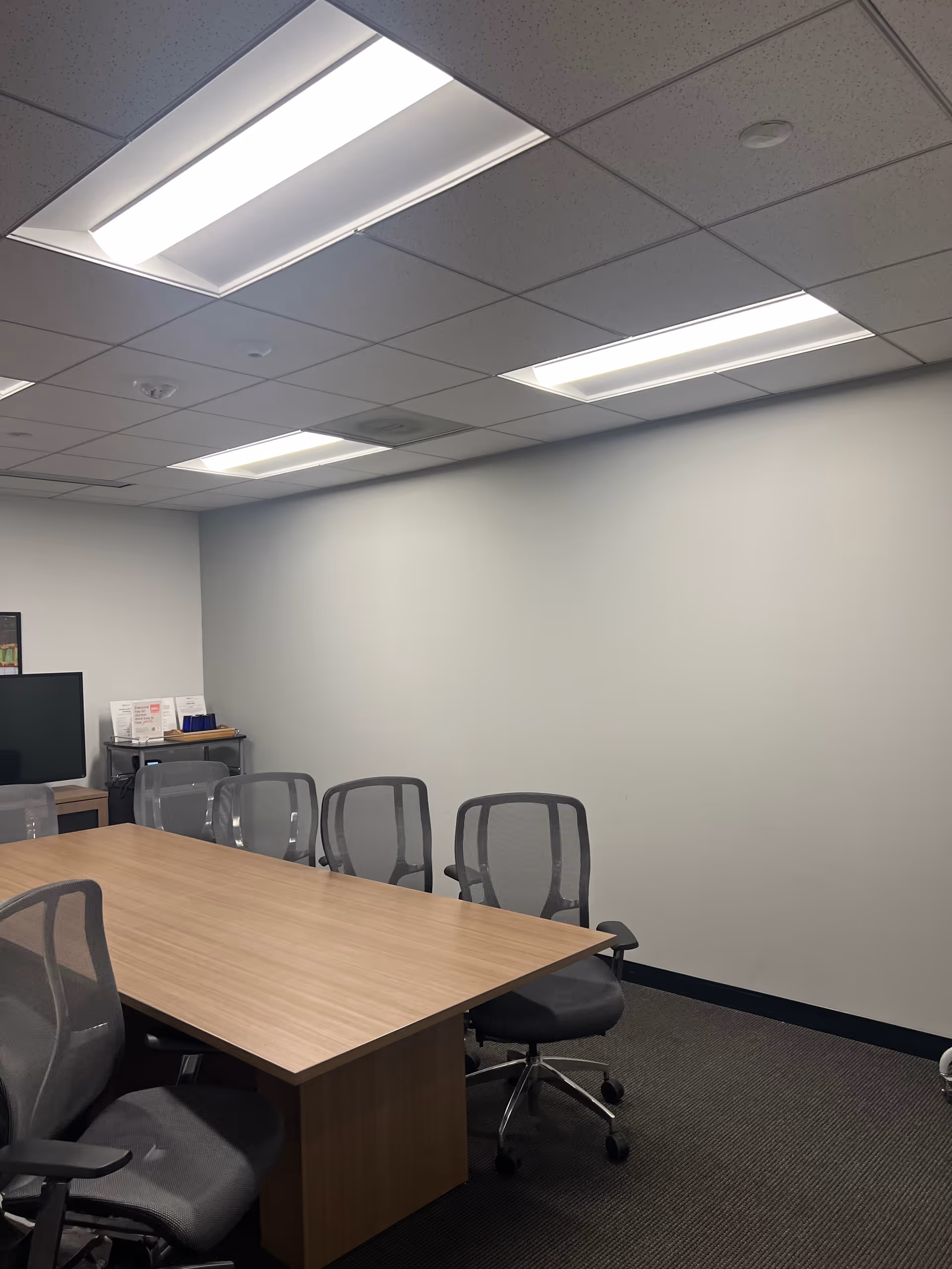 A conference room with a wooden table and gray office chairs under ceiling lights.