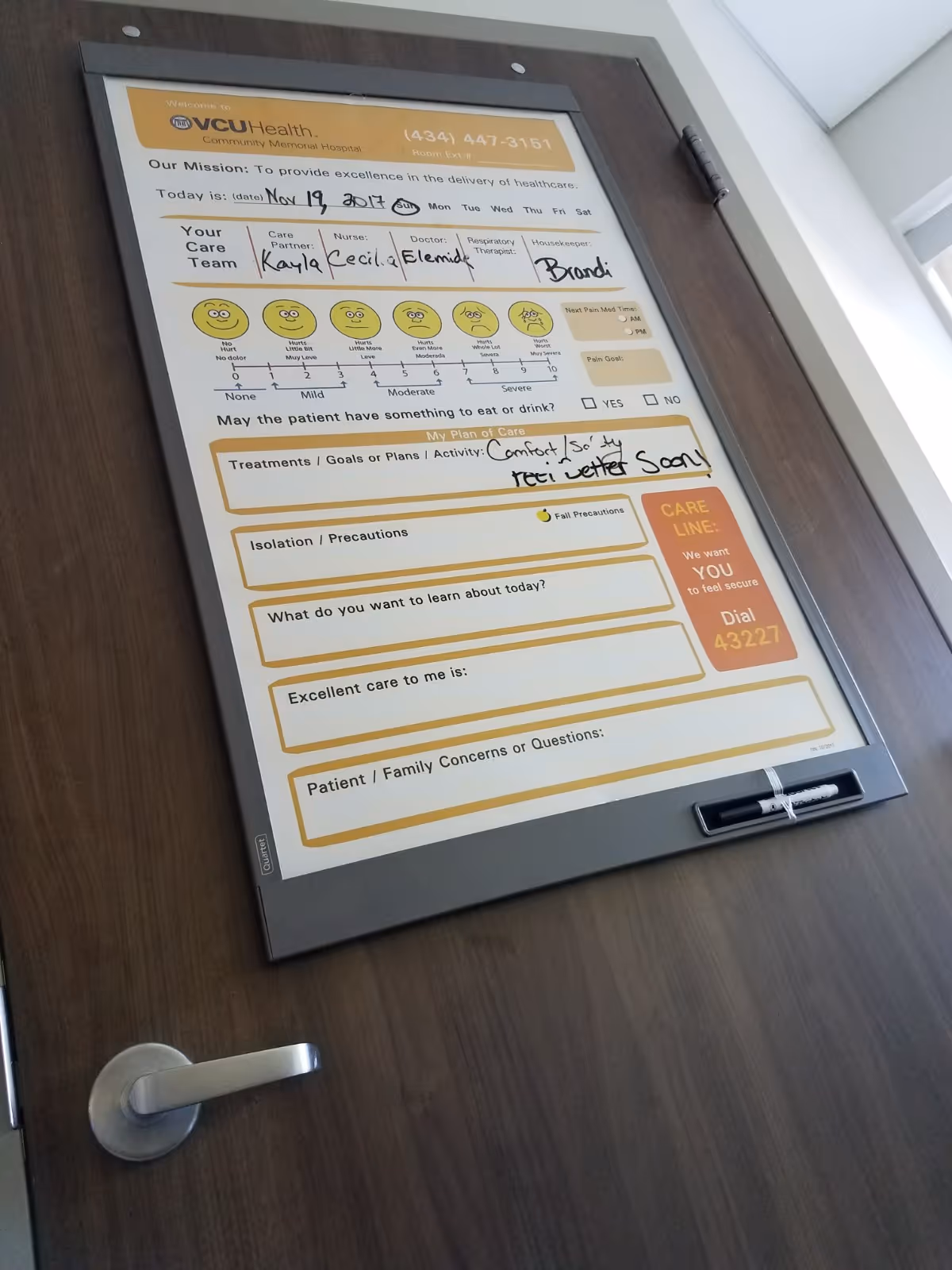 Framed patient care plan board mounted on a wooden door in a hospital corridor.