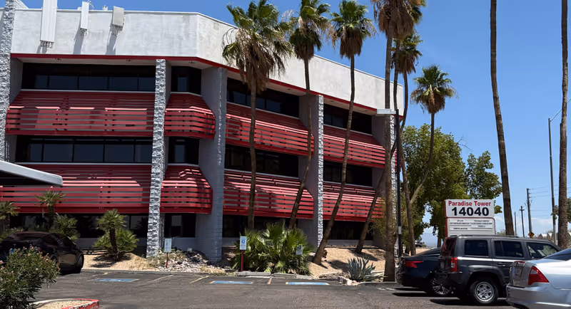 Exterior of a multi-story building with red balconies and tall palm trees