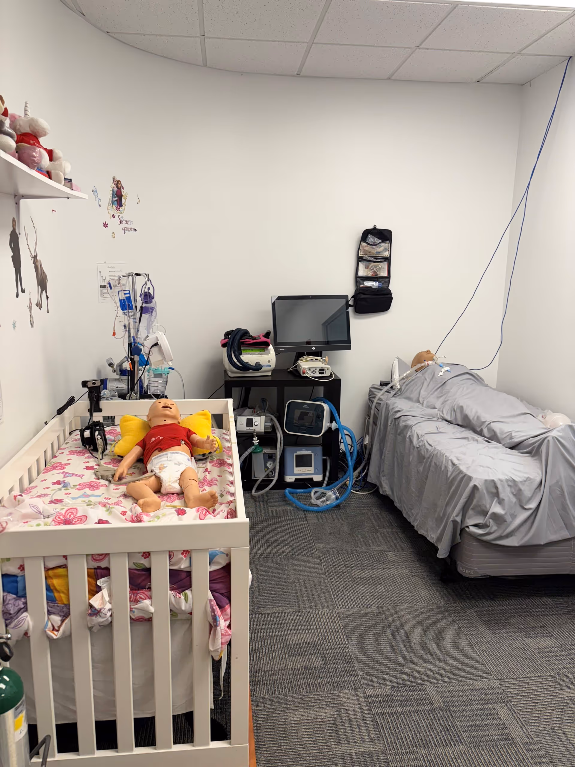 Pediatric clinical room with a baby mannequin in a crib and medical equipment.
