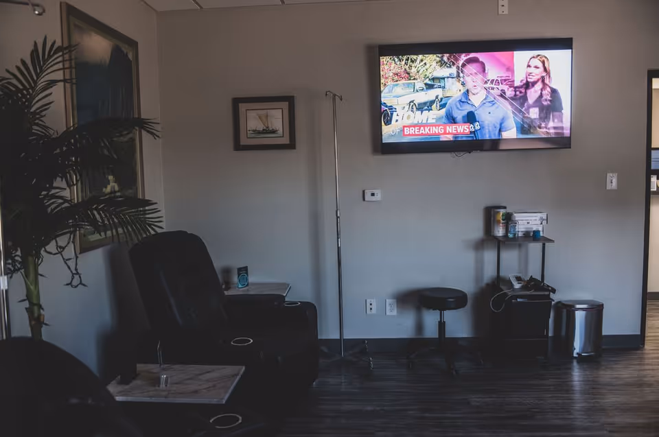 Interior lounge area with wall TV, reclining chair, IV pole, and plant decor.