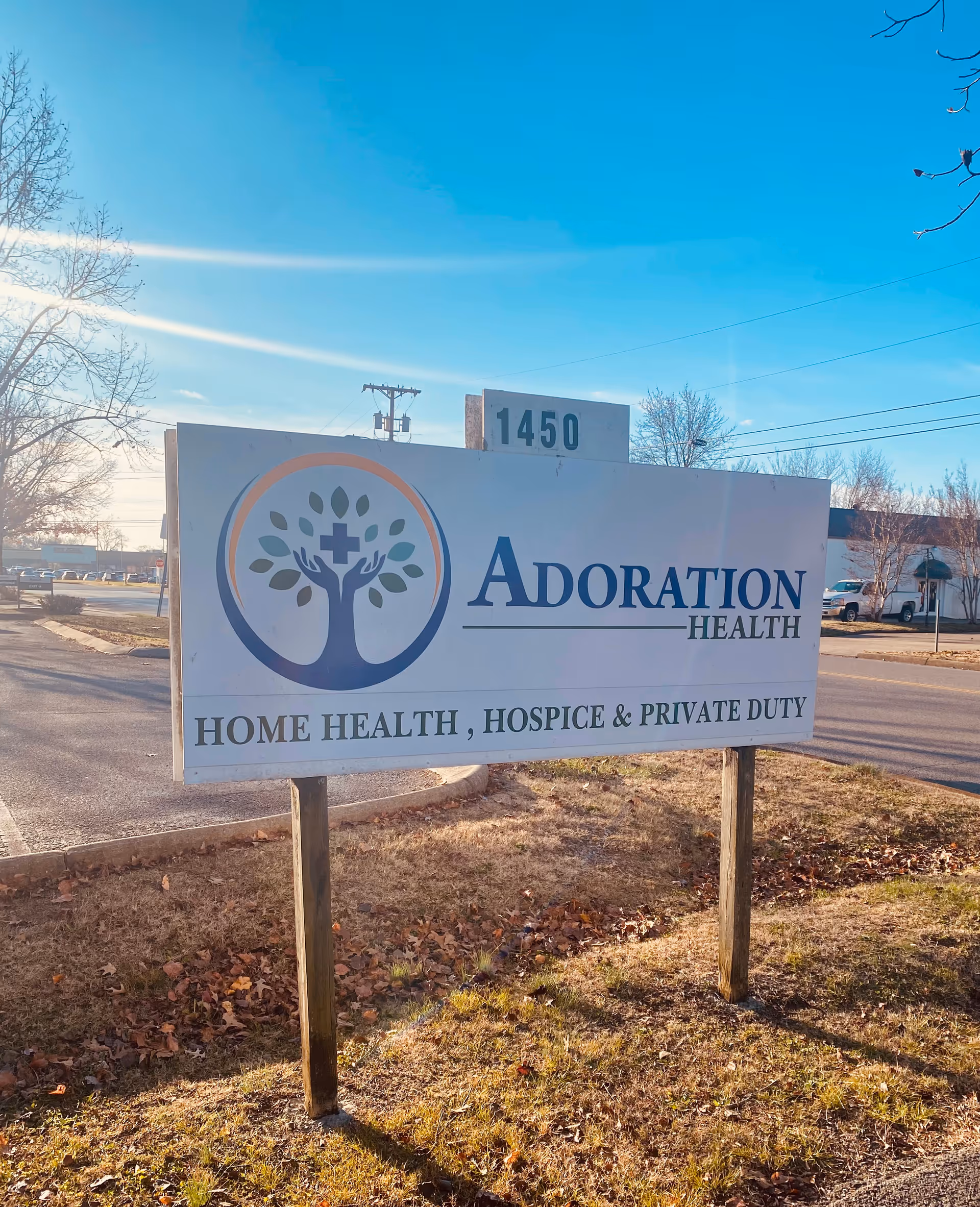 Roadside sign for Adoration Health, stating Home Health, Hospice & Private Duty, under blue sky.
