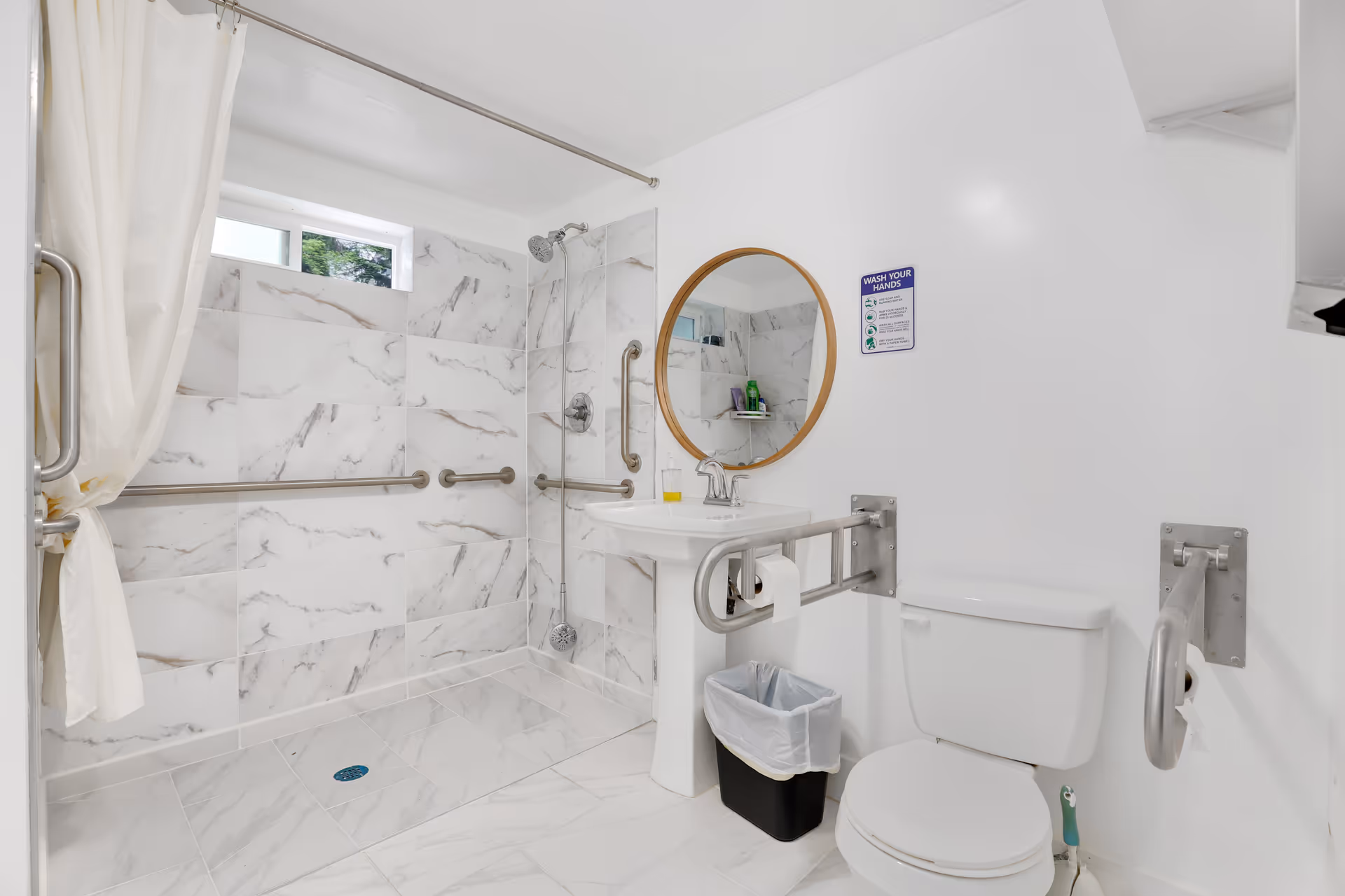 Accessible bathroom with marble tiles, shower, grab bars, sink, mirror, and toilet.