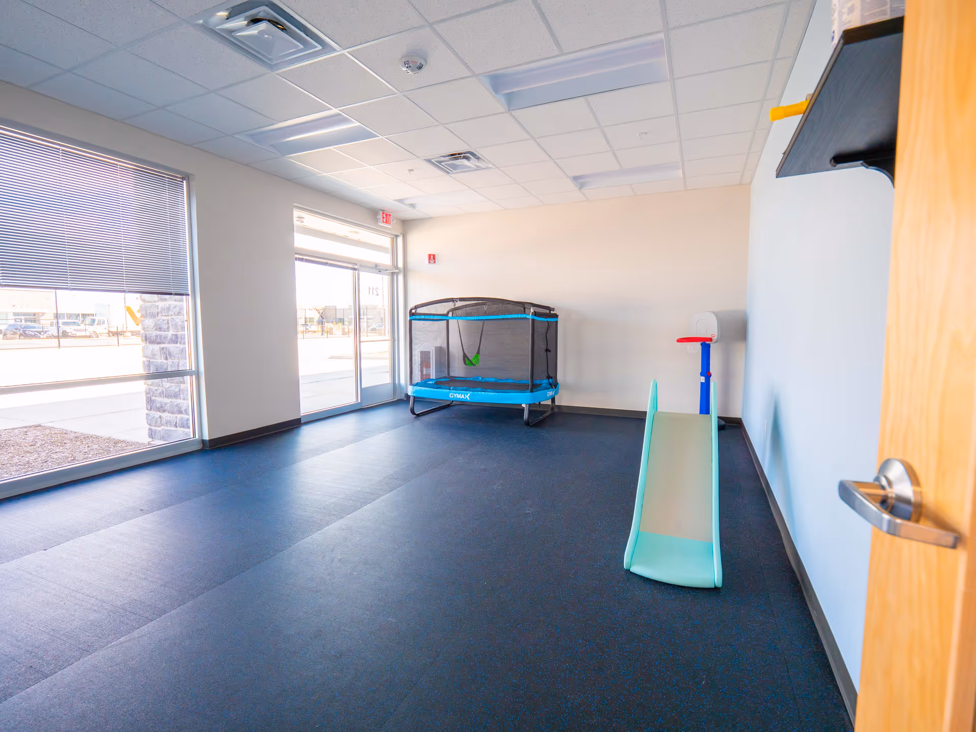 Bright indoor play area with a trampoline and small slide near large viewing windows.