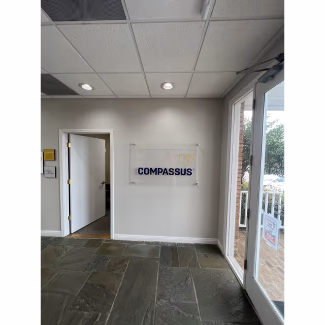 Lobby area with Compassus sign on the wall, doorway, glass entrance door, tiled floor.