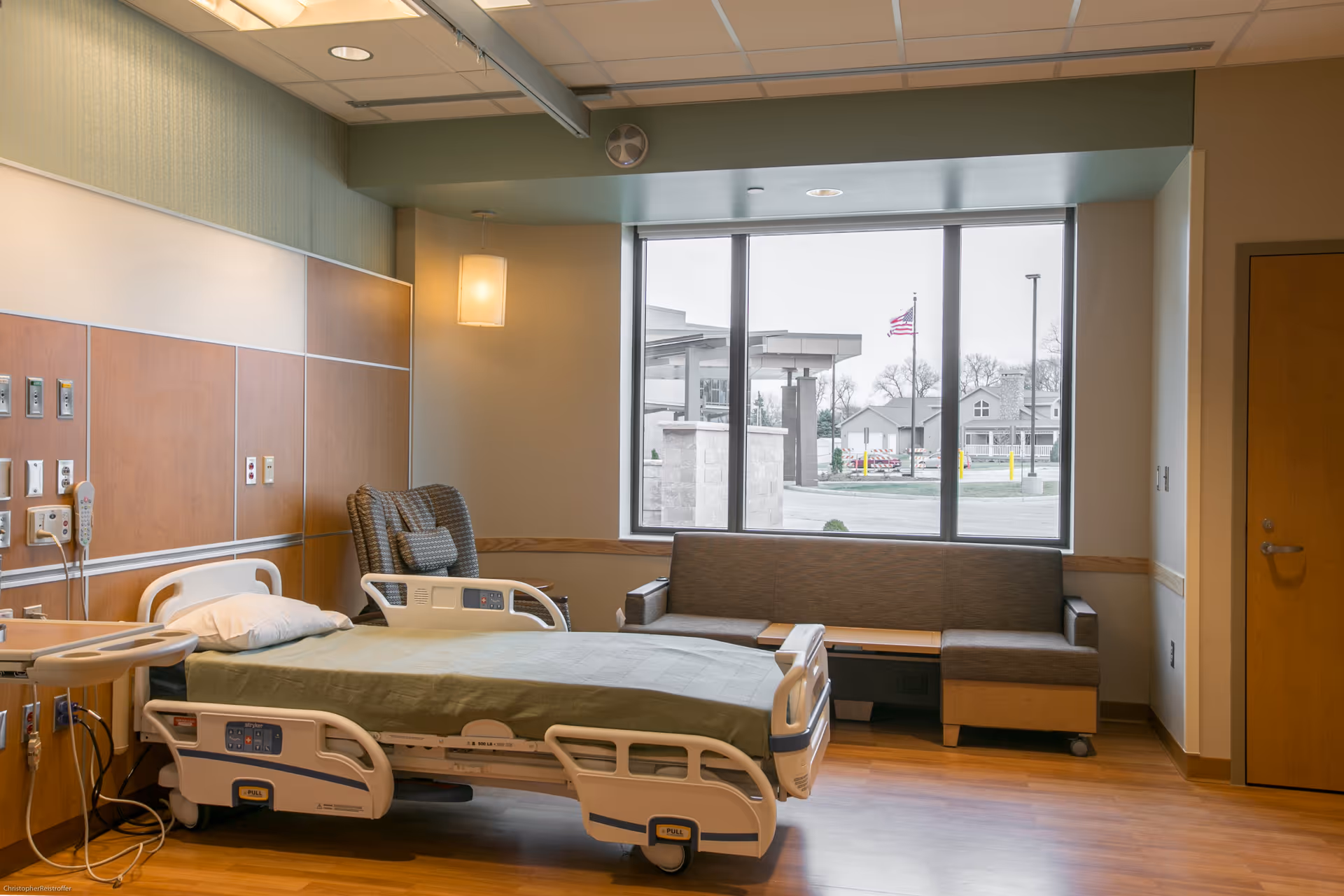 Hospital room with adjustable bed, seating area, and large window.
