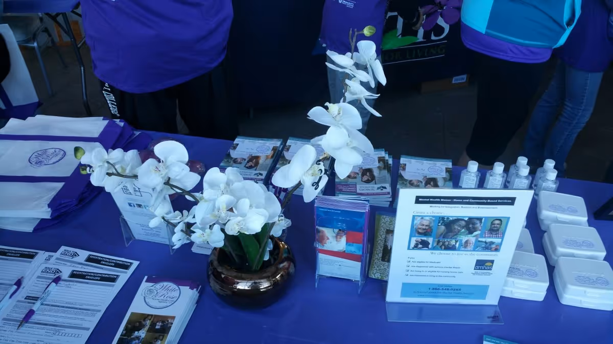 Promotional booth with brochures and white orchids on a purple table indoors.