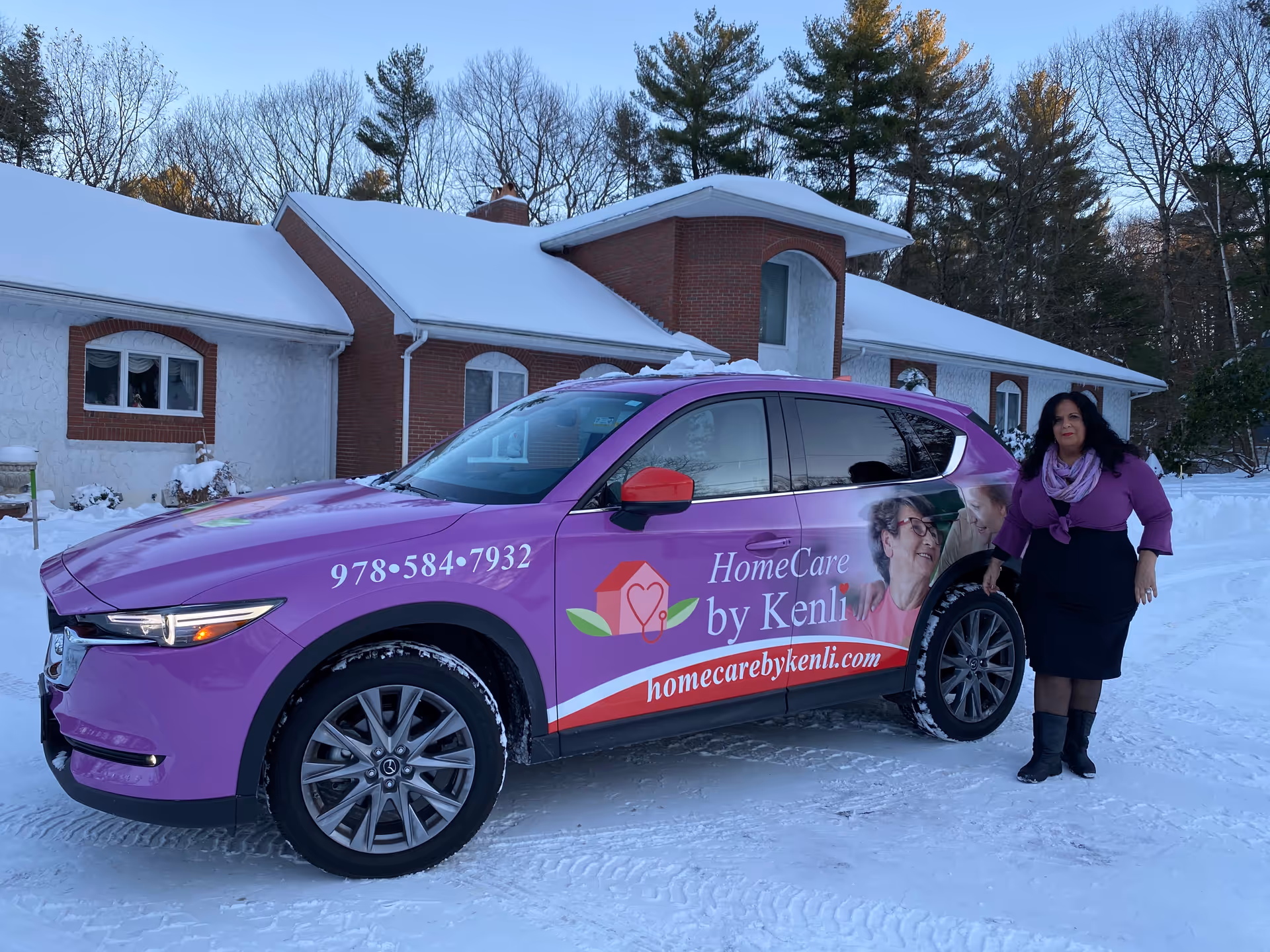 Purple HomeCare by Kenli vehicle parked outside a snow-covered building, with a woman beside it.