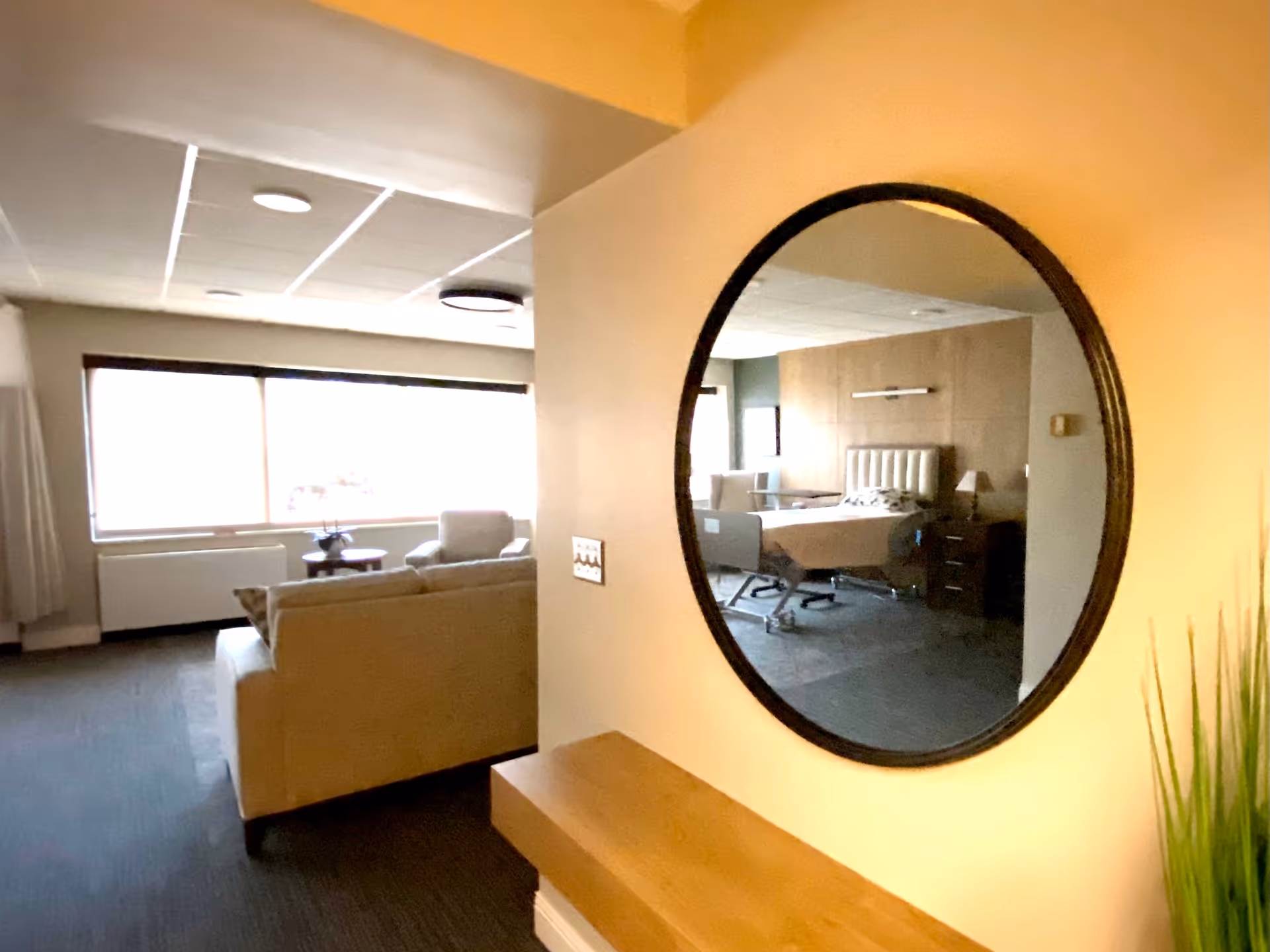 Lounge area with sofa, round mirror, and a reflected bedroom scene.
