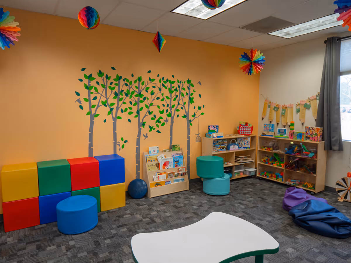 Bright, child-friendly playroom with colorful blocks, shelves of toys, and a tree mural.