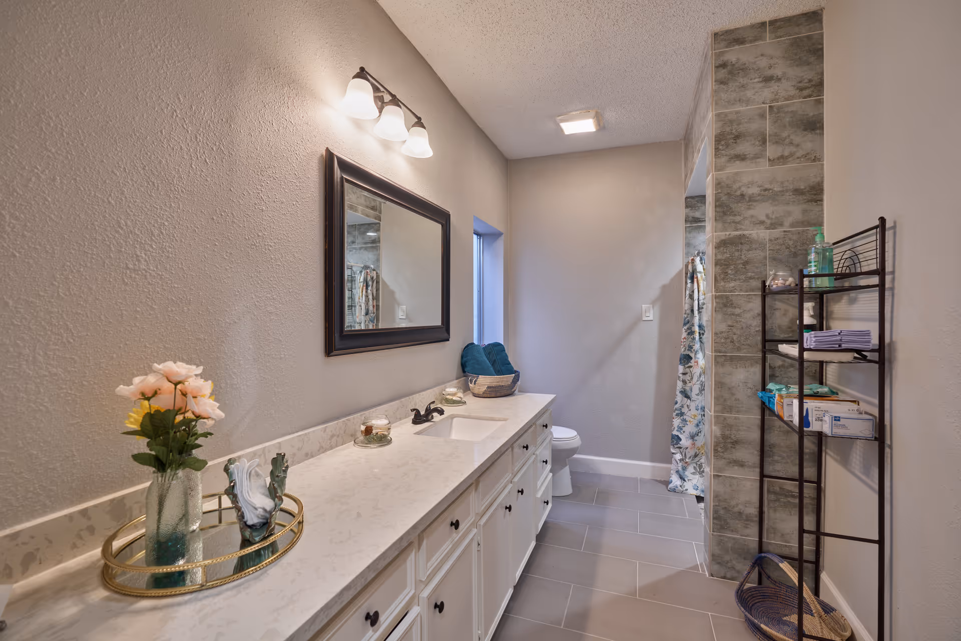 Long bathroom vanity with marble countertop, mirror, and shower area in a neutral-lit room.
