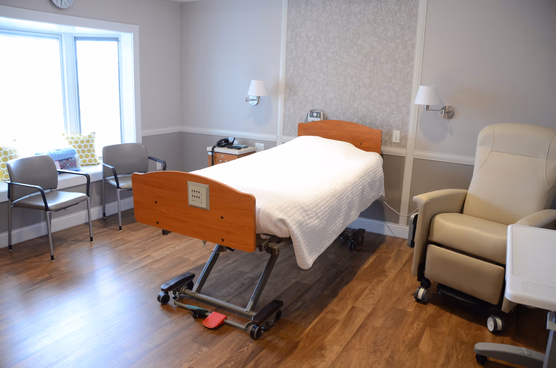 Hospice patient room with adjustable bed, recliner, and window seating.