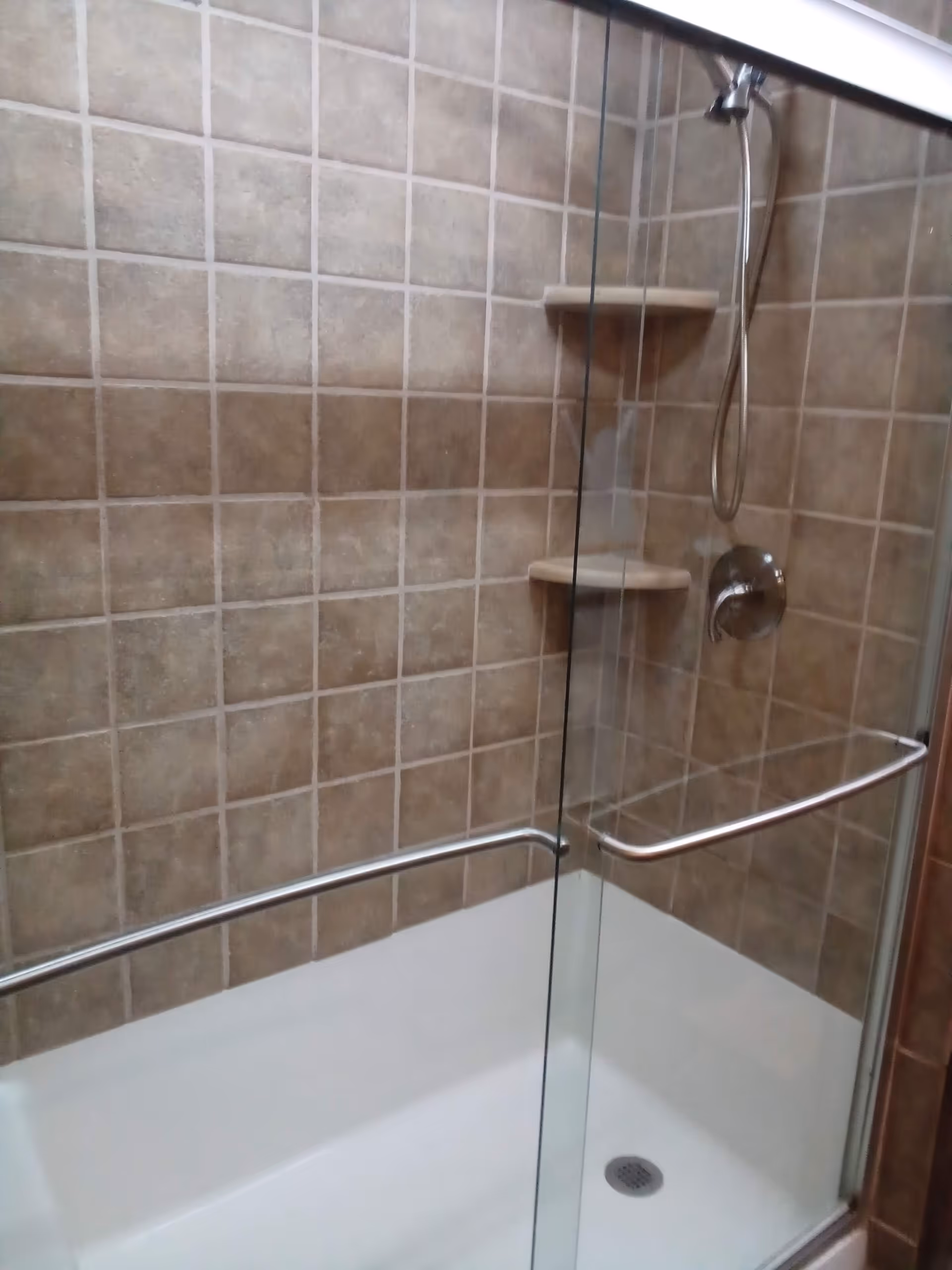 Shower stall with glass door, tiled walls, and metal grab bars.