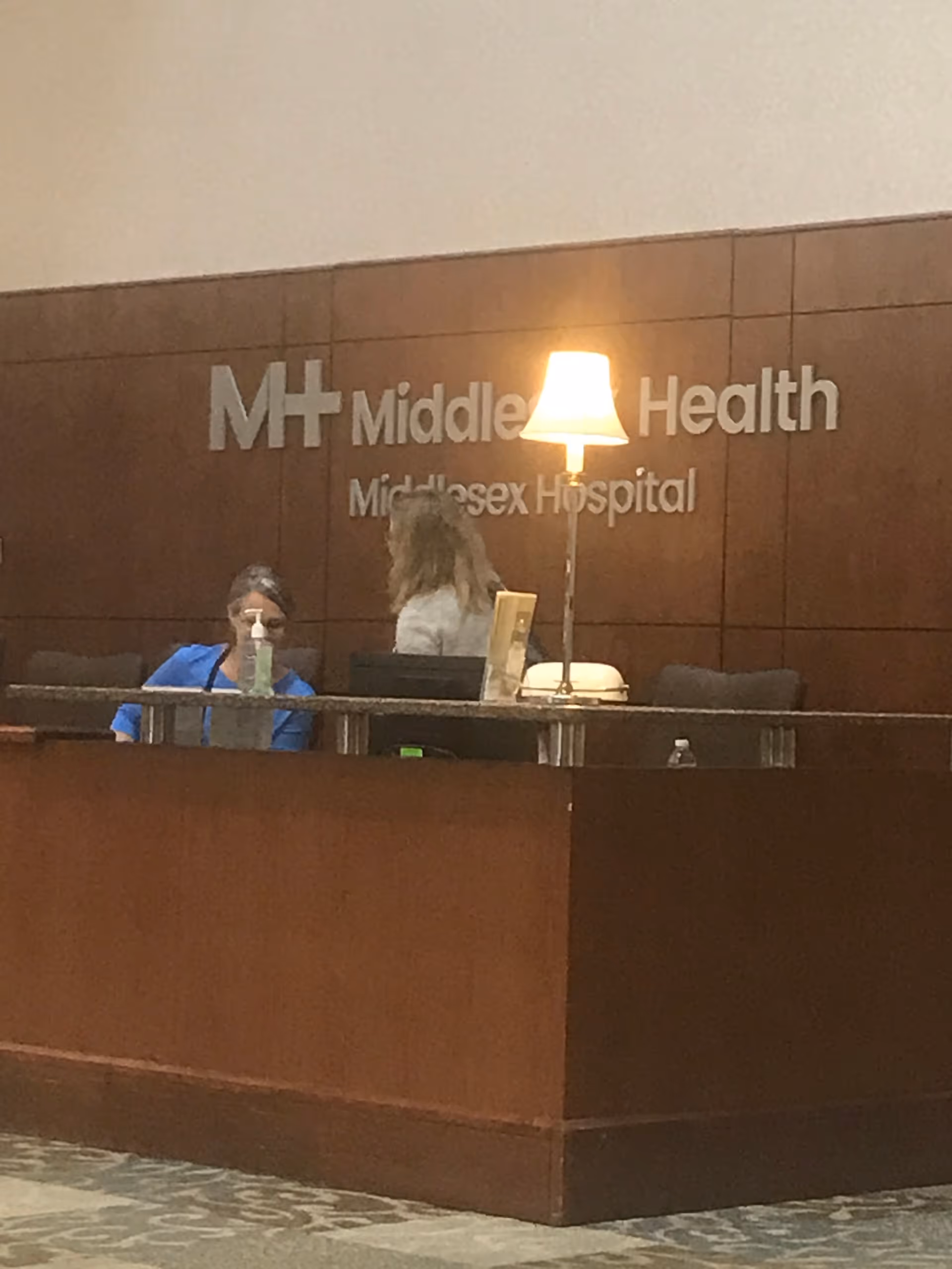 Hospital lobby desk with 'Middlesex Health' sign on wood paneling.