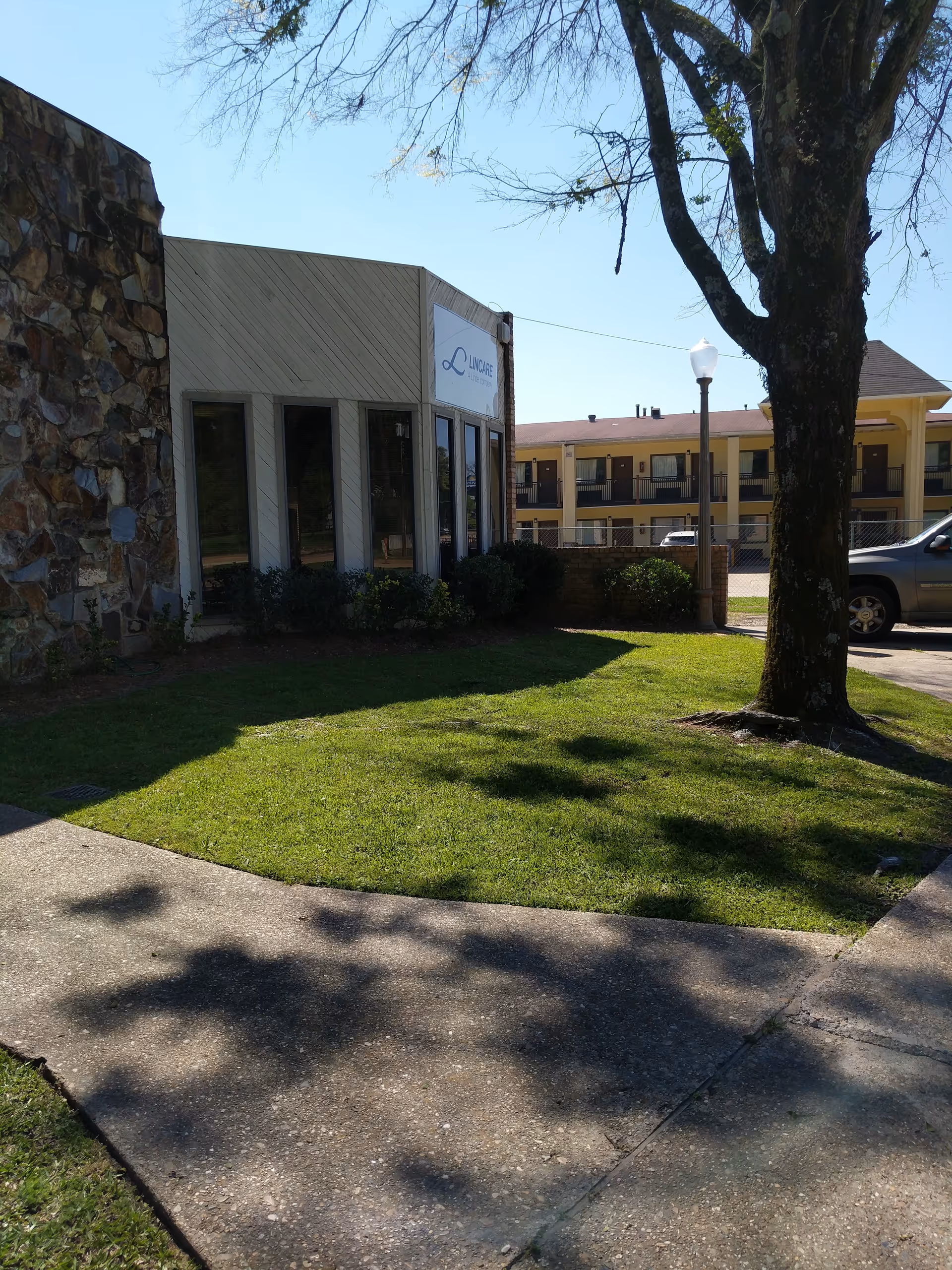 Exterior view of LINCARE facility with lawn, tree, and adjacent building.