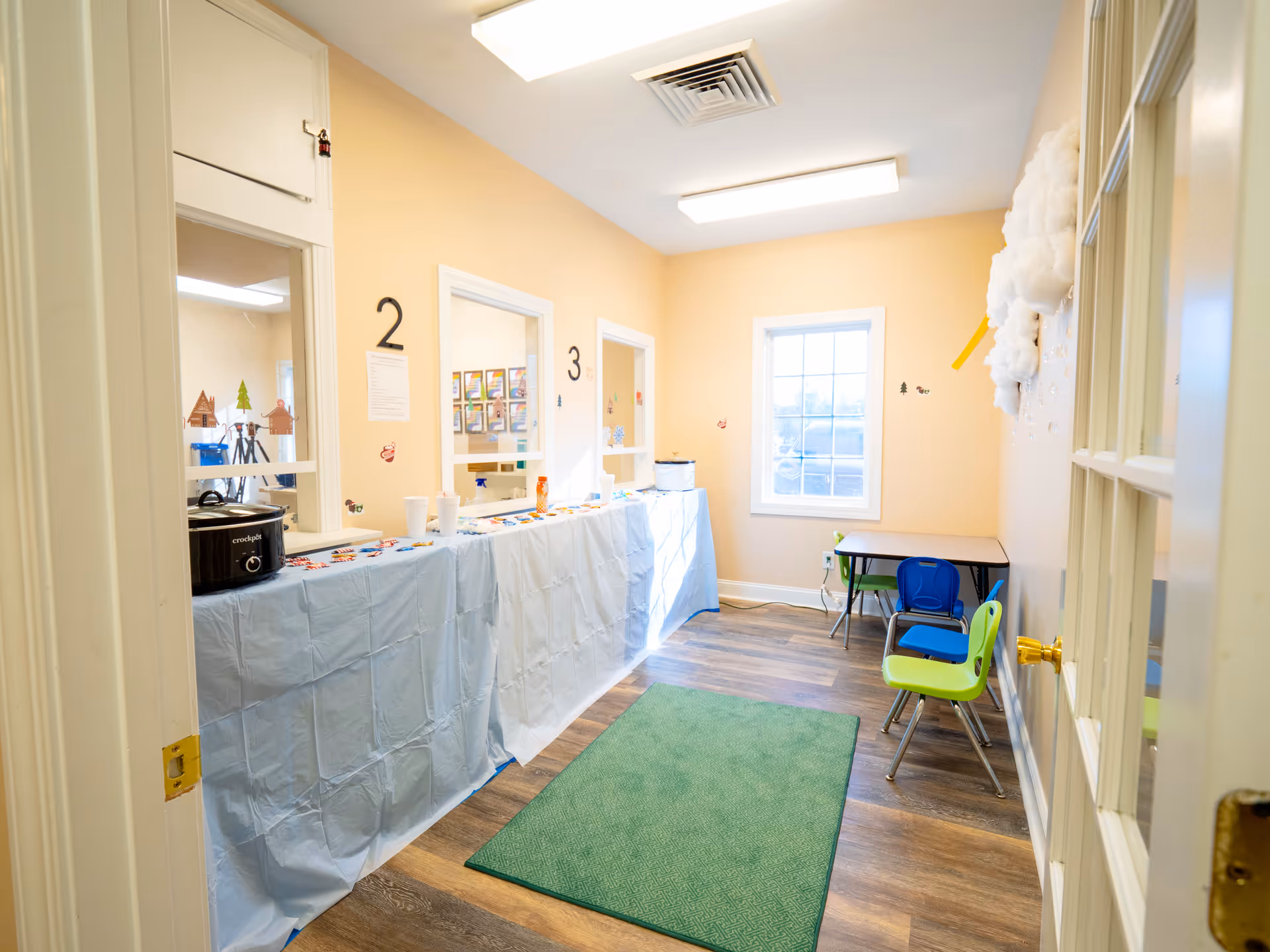 Interior of an activity room with a long table covered in blue cloth and bright chairs.