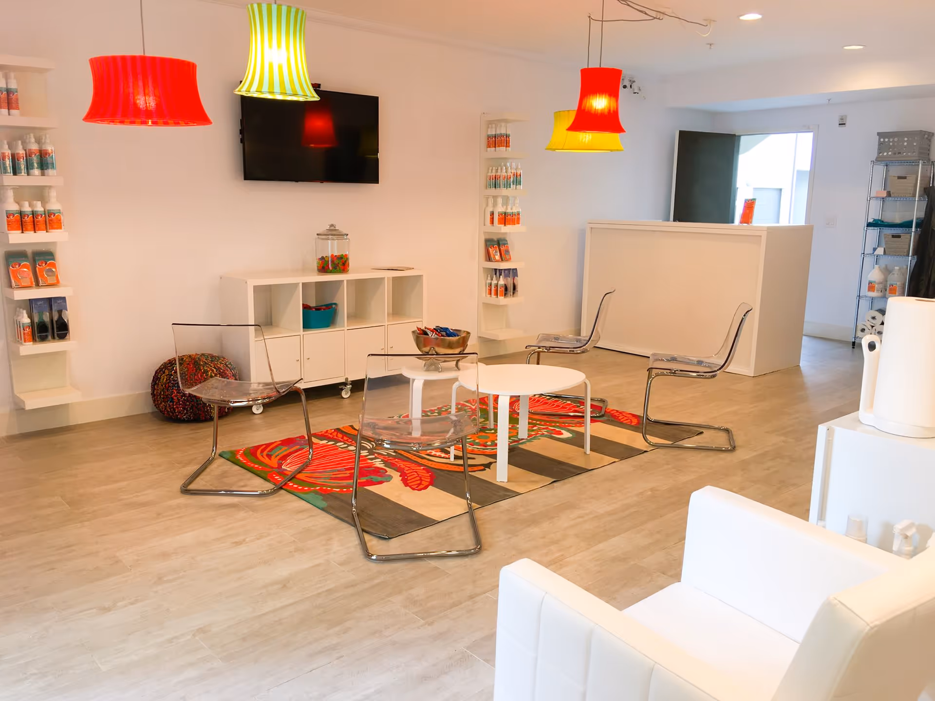 Bright modern lounge with white furniture, colorful pendant lights, a TV, and a reception desk.